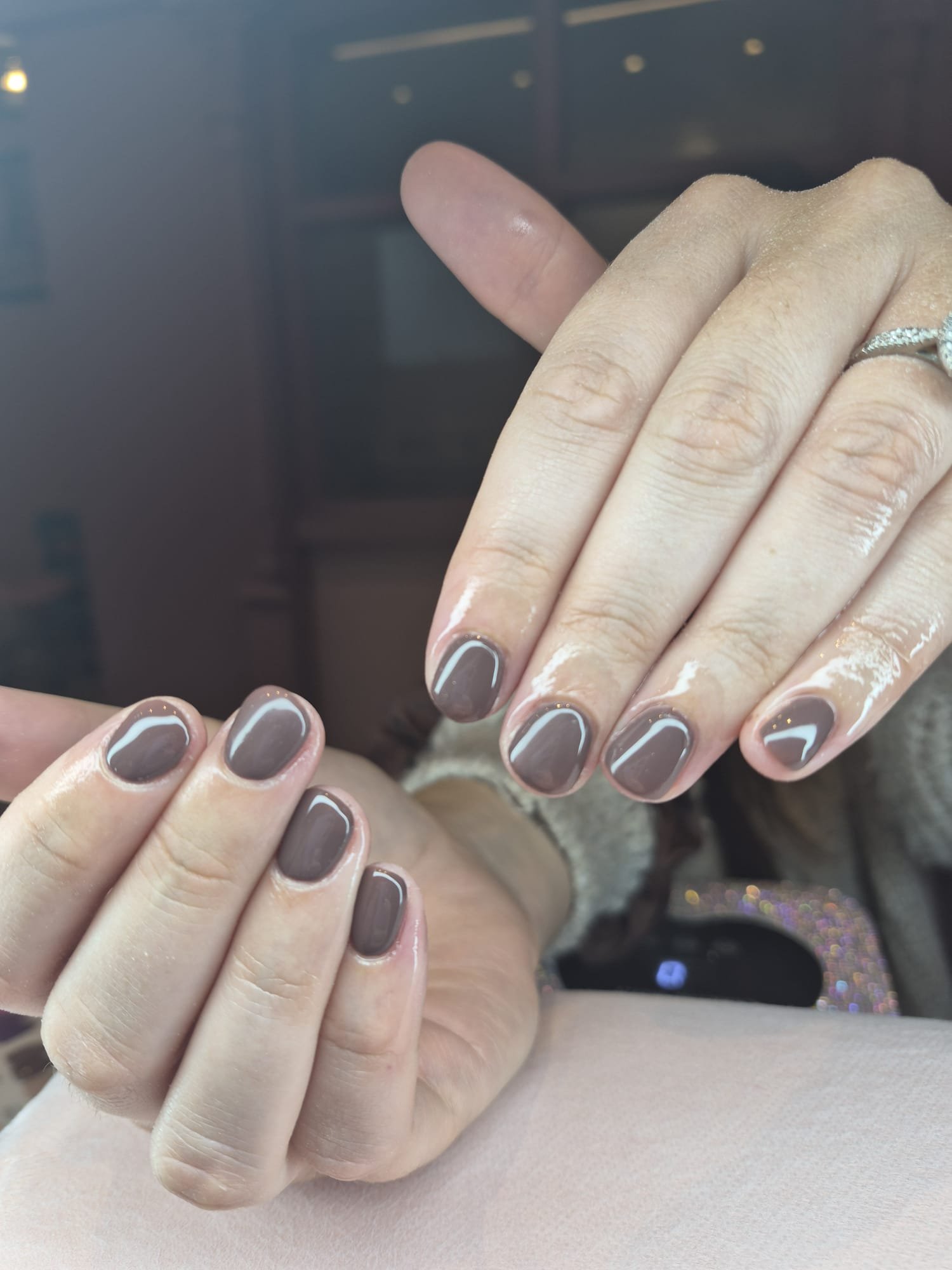 Close-up view of a person's hand with freshly manicured nails painted in taupe with white accents, wearing a silver ring with small stones.