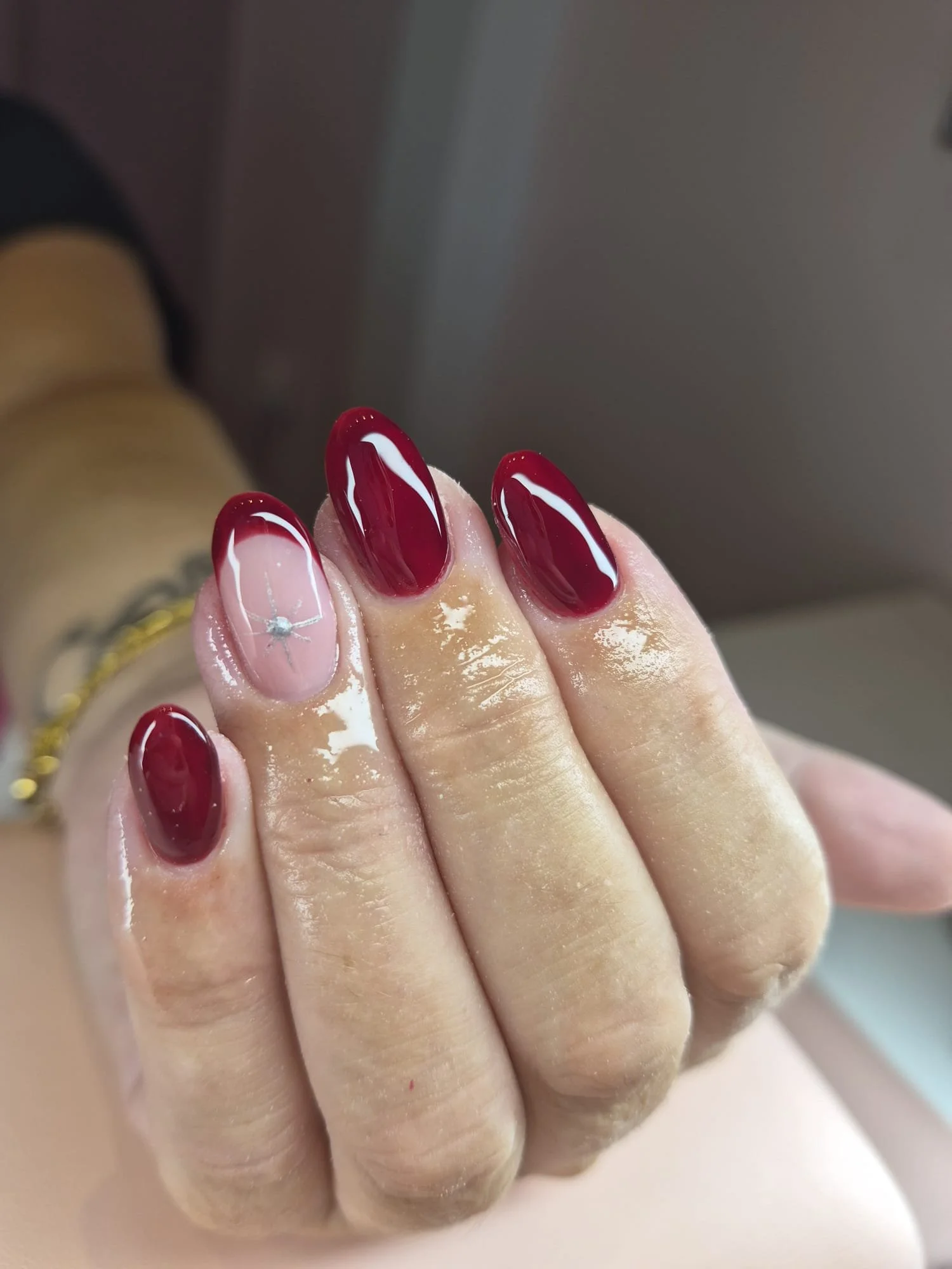 Close-up of a person's hand with long, oval-shaped nails painted in red with white swirl designs, fingers slightly bent, and jewelry around the wrist.