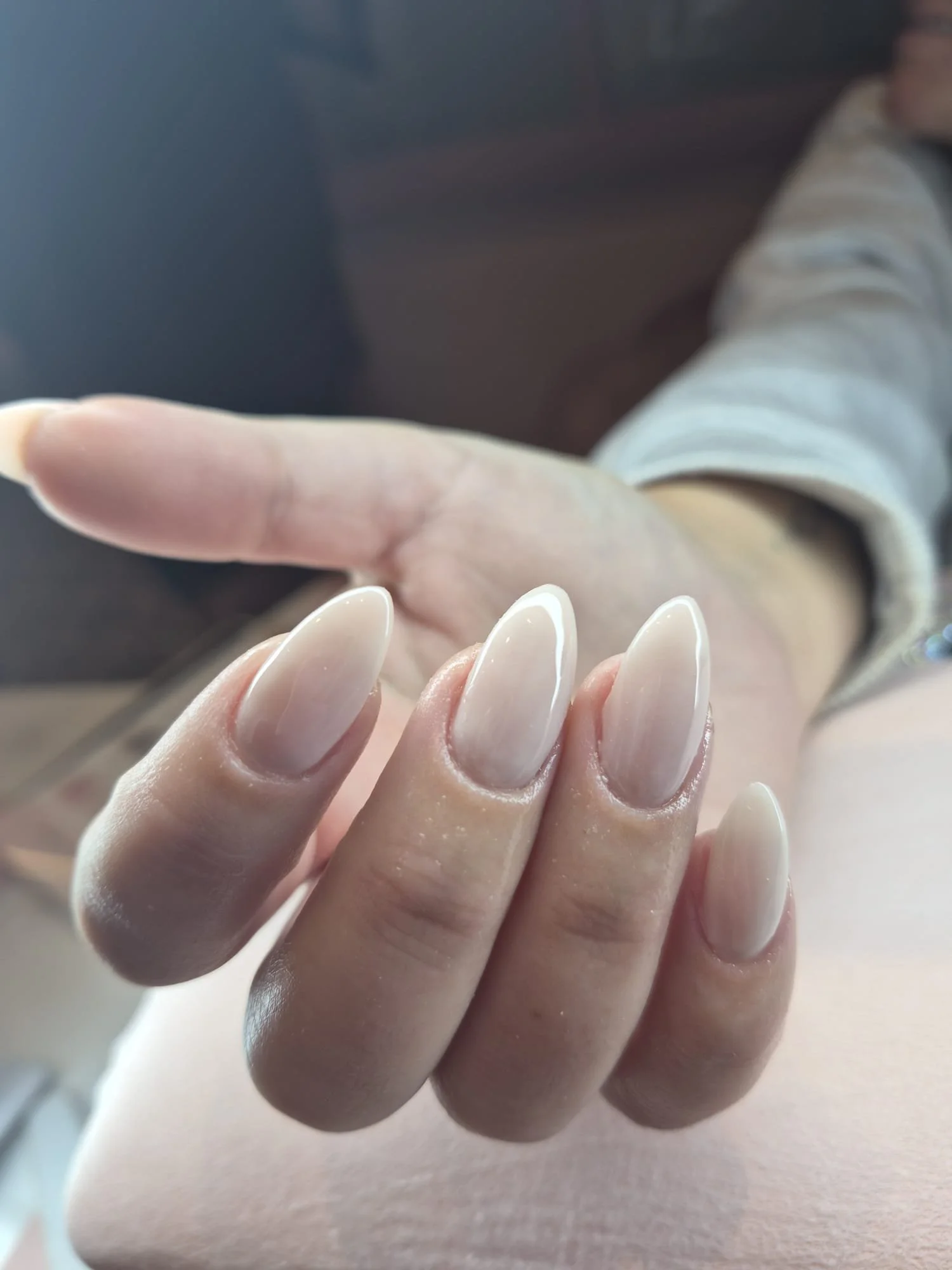 Close-up of a hand with well-manicured, shiny white nails, person wearing a light-colored long-sleeve top, background blurred.