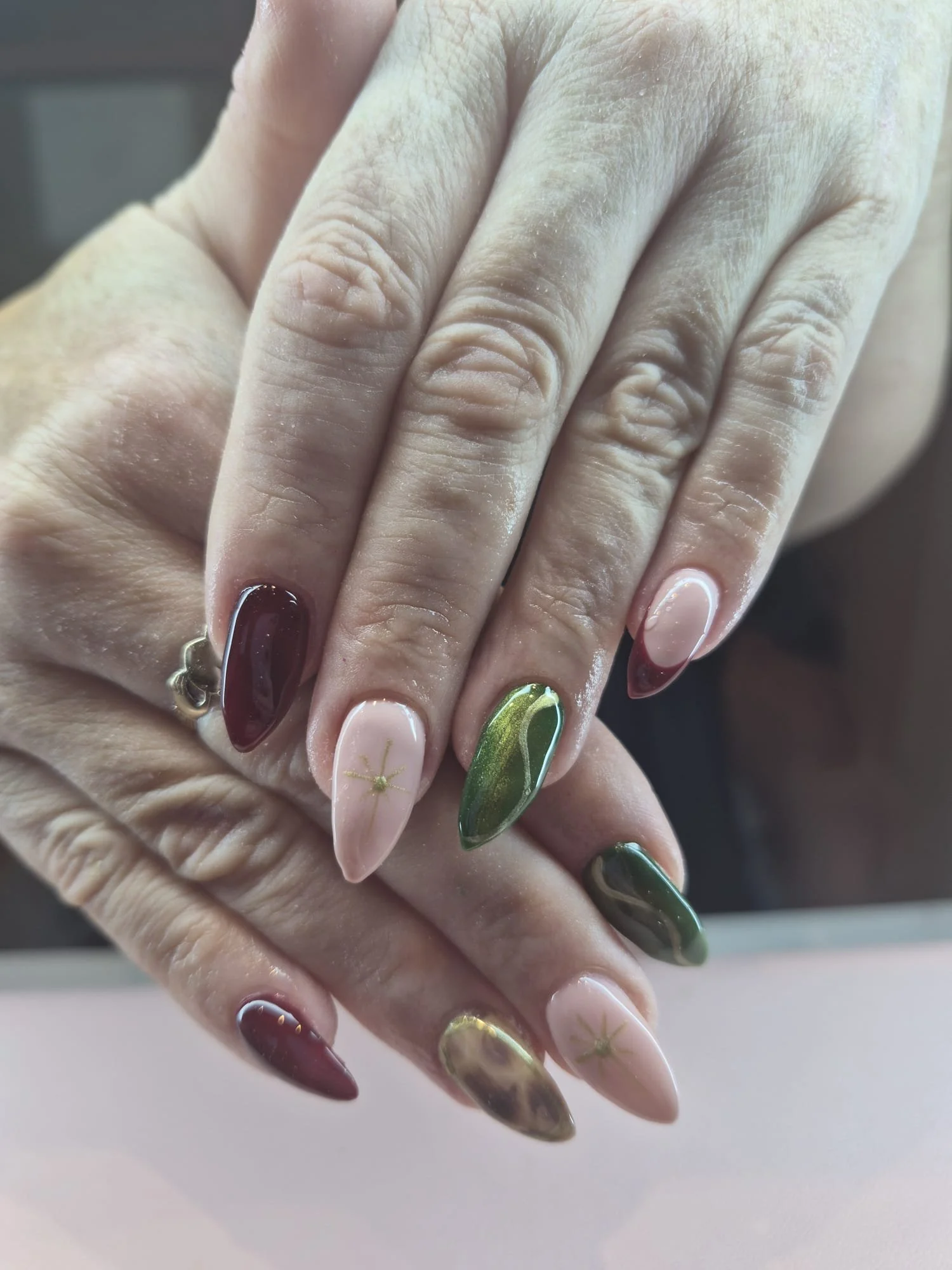 Close-up of a person's hand with manicured nails in various colors and designs, including maroon, pink with gold, green with gold, and a neutral shade.