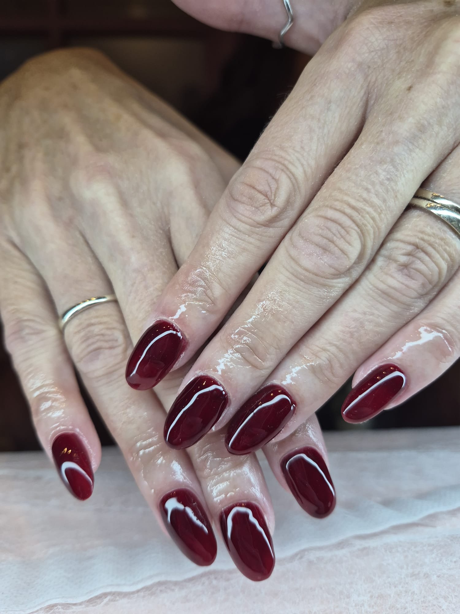 Close-up of hands with red and white decorated fingernails, wearing rings, with a shiny gel manicure.