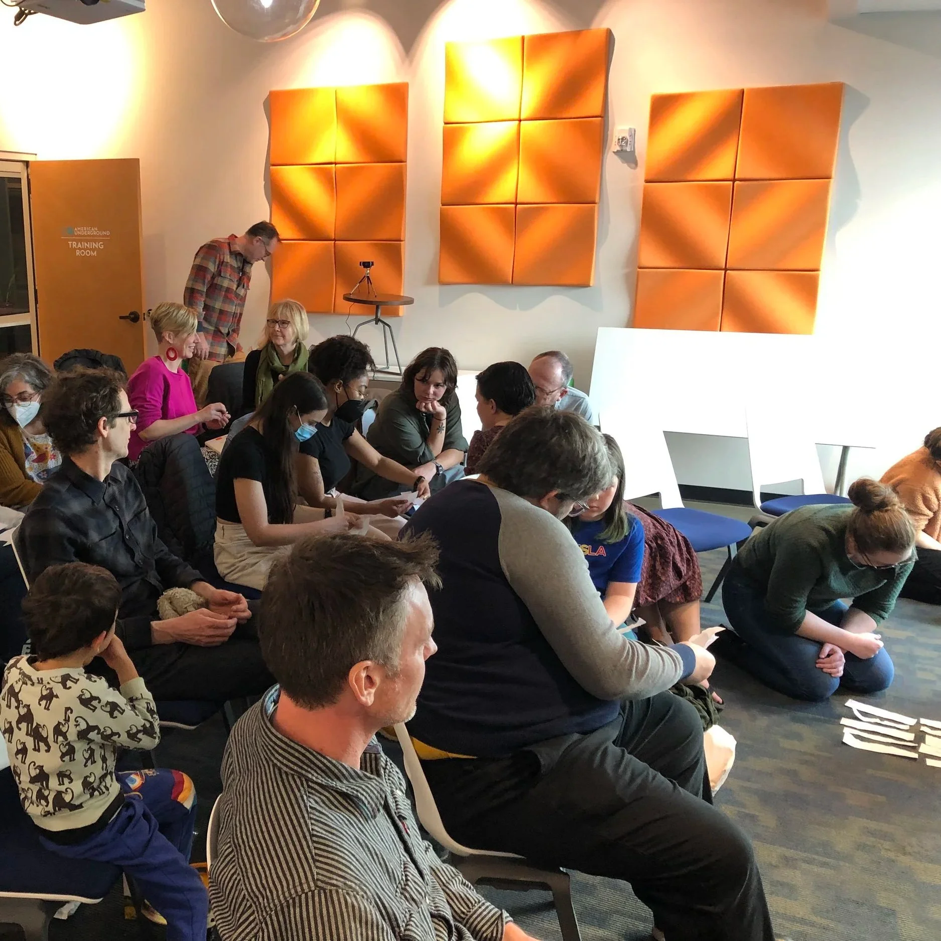 People sitting and kneeling on chairs in a conference room during a meeting or presentation.
