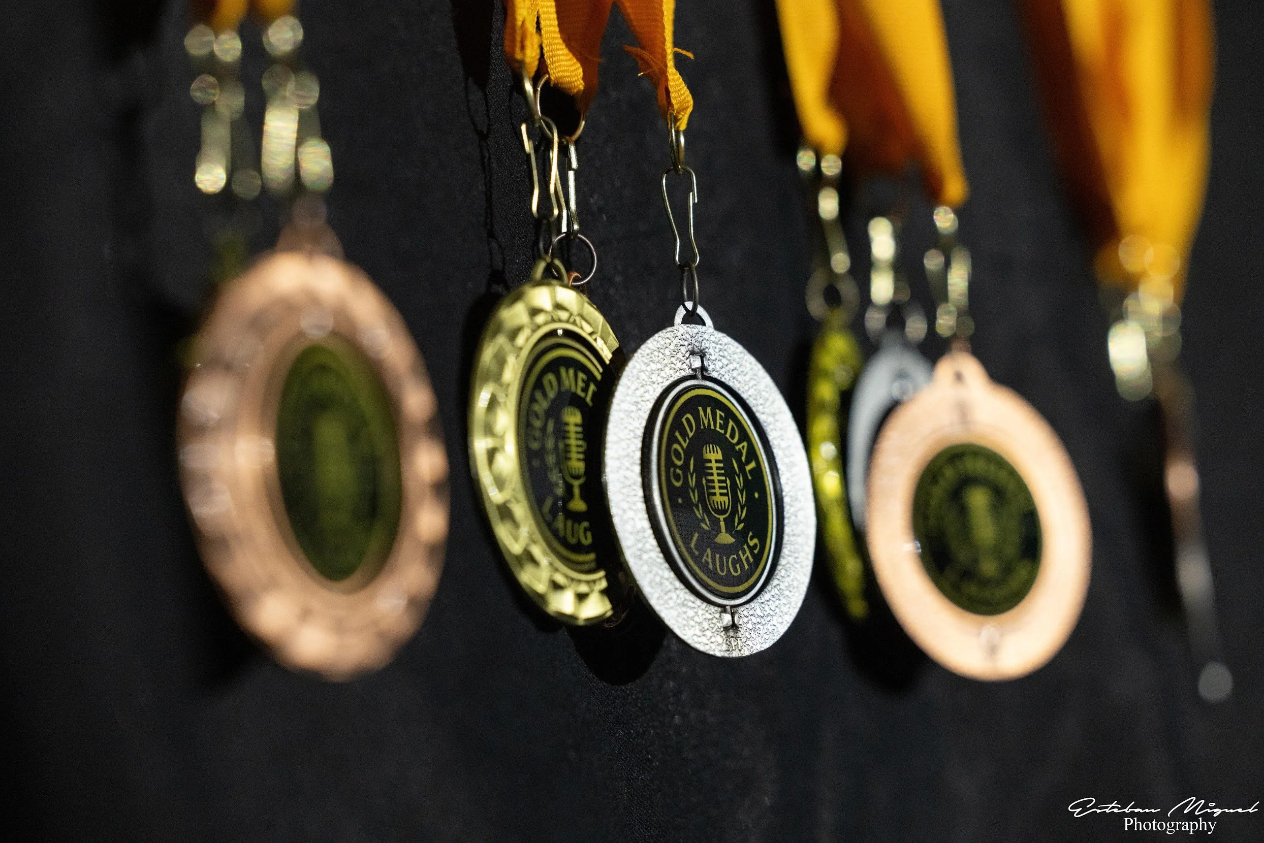 Several medals hanging from yellow and black ribbons, with a black background.