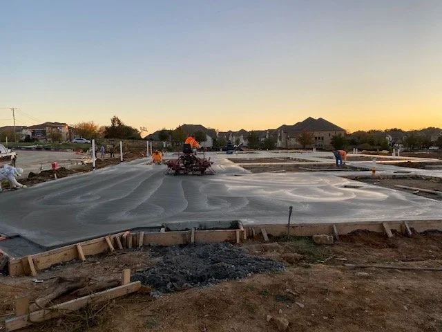 Construction workers pouring concrete for a building foundation during sunset.
