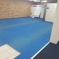 Indoor sports facility with blue padded flooring and whiteboards or scoring boards in the background.