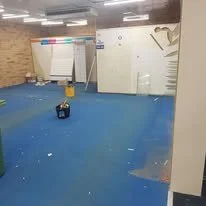 Empty gym with blue flooring, white walls, exercise equipment, and a weightlifting bench in the background.