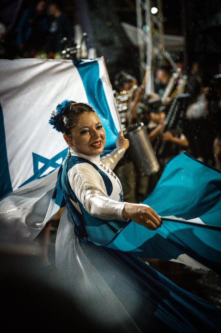 Mujer vestida con los colores de la bandera de Israel, sosteniendo una bandera en un desfile o celebración.