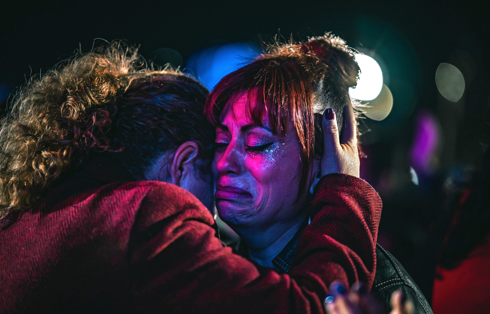 Dos mujeres se abrazan emocionalmente en un momento de consuelo y tristeza en un entorno oscuro.