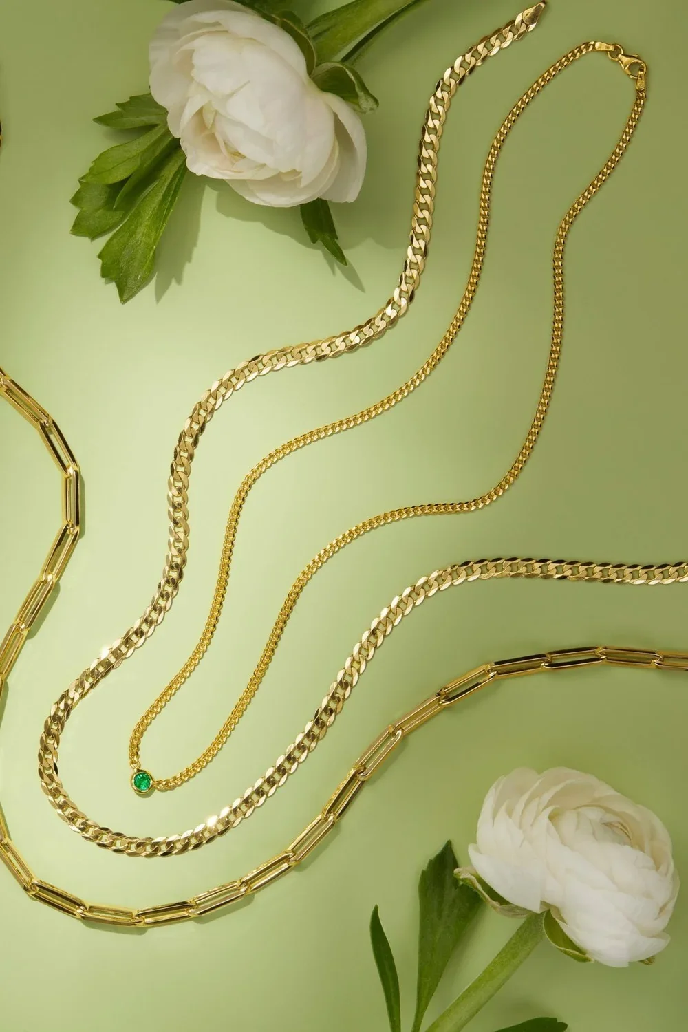 Gold jewelry necklaces on a light green background with white peony flowers and green leaves.