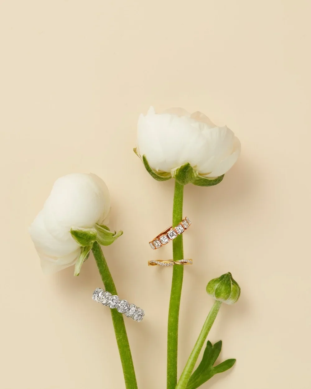Three white flowers with green stems, each adorned with a different ring, against a light background.
