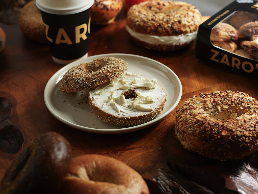 Assorted bagels with cream cheese and a to-go coffee cup on a wooden table