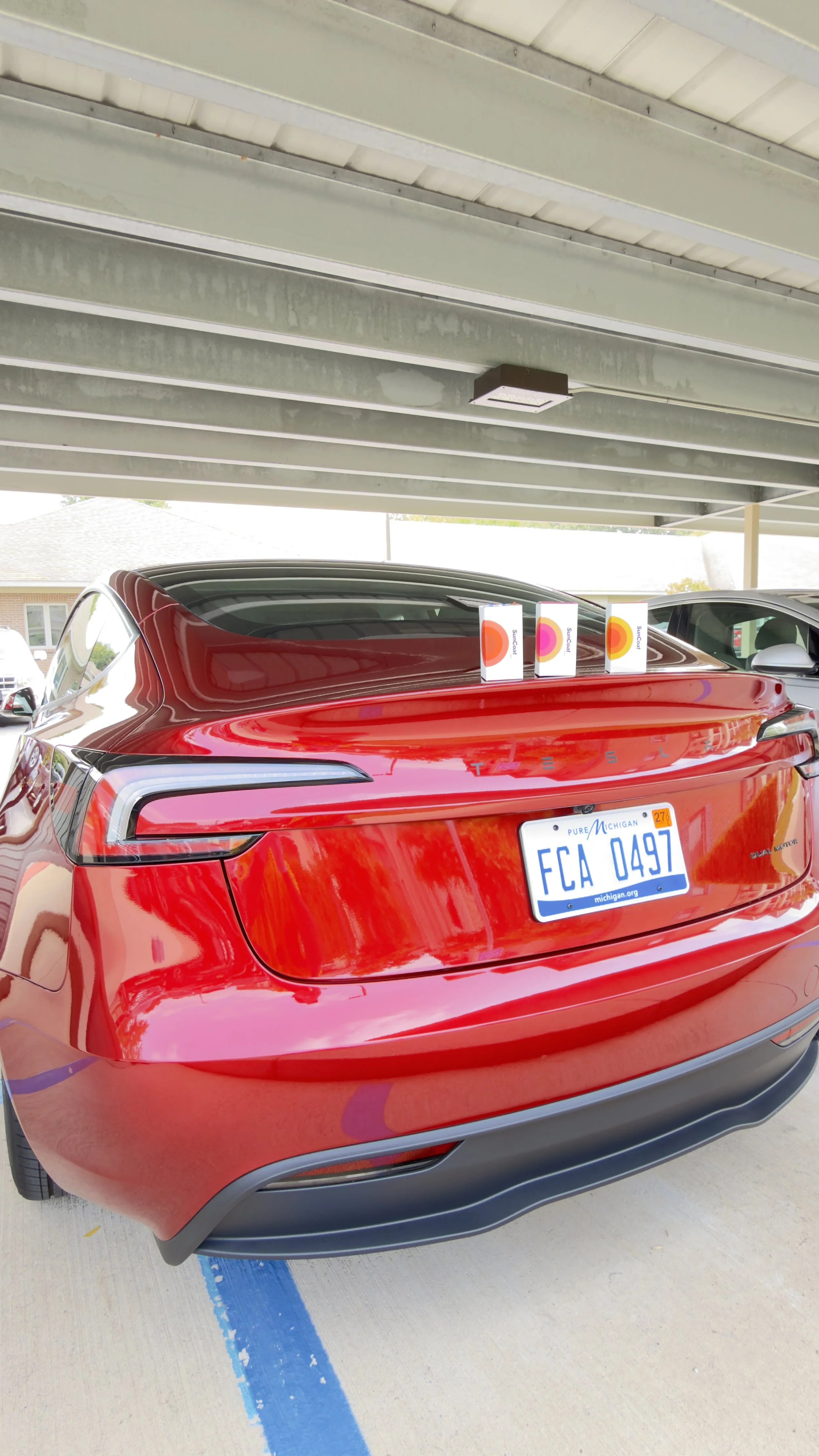 Red Tesla Model Y parked under a parking structure with three boxes of Suncor products on its back.