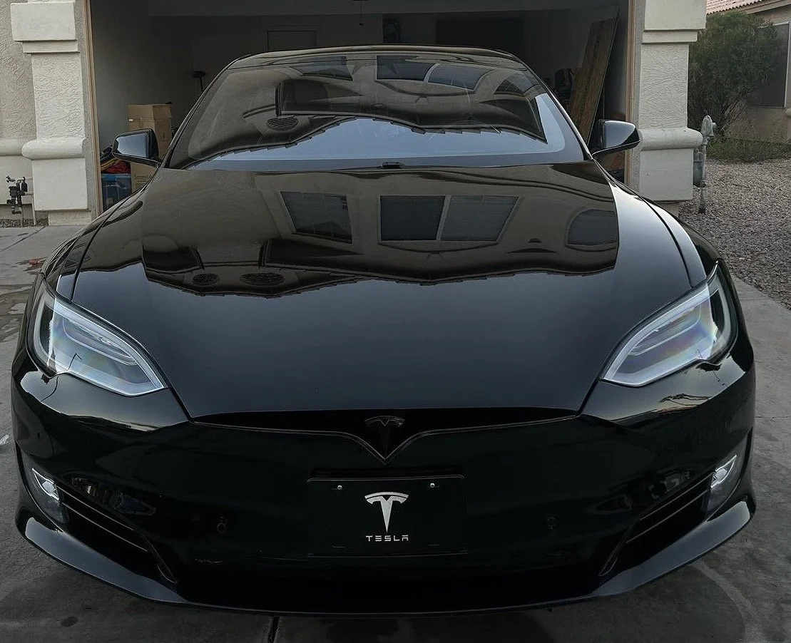 Front view of a black Tesla Model S parked in a driveway, with a garage and house in the background.