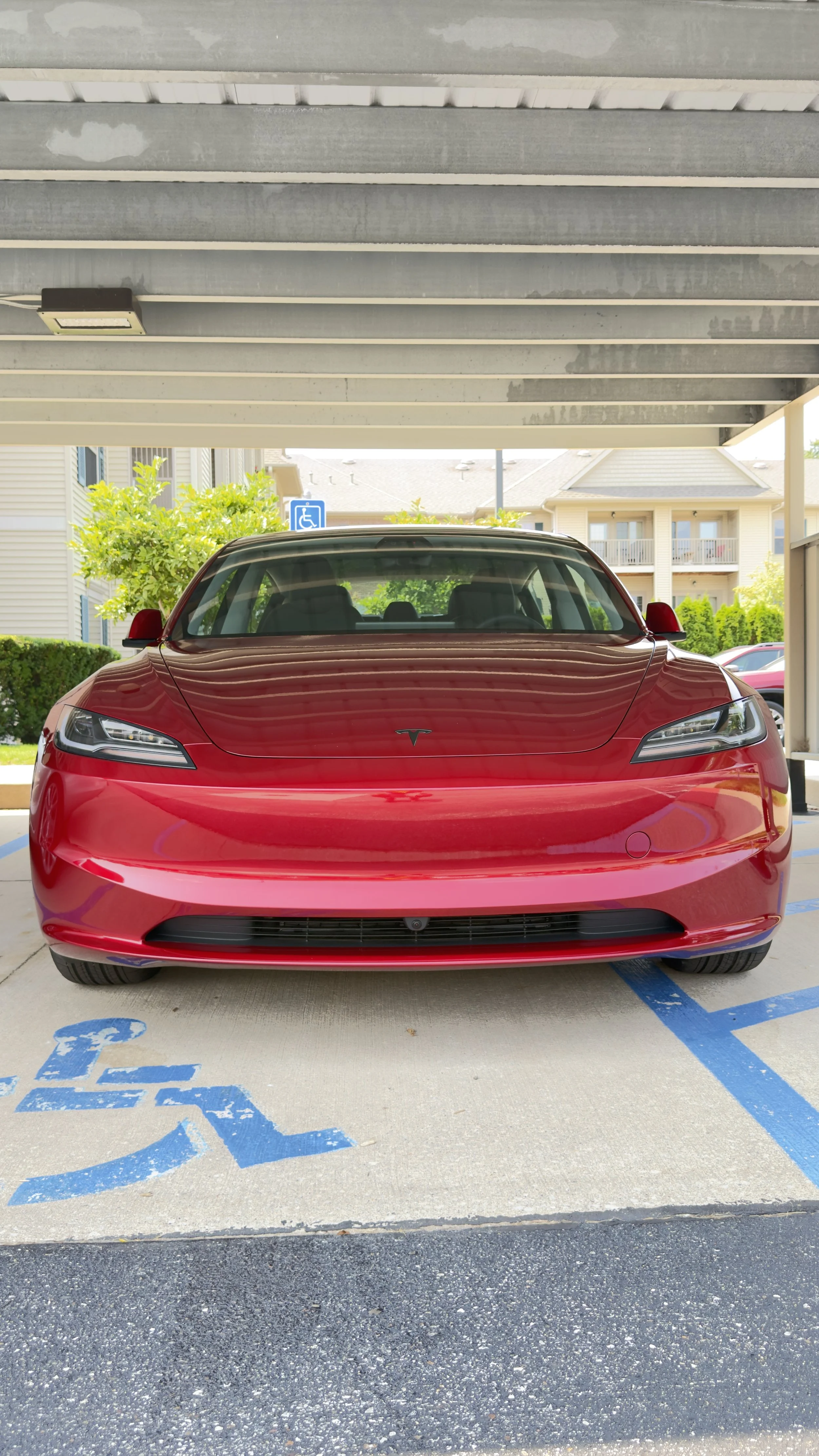 Red Tesla car parked in a designated handicapped parking space under a parking structure with a handicap sign visible in the background.