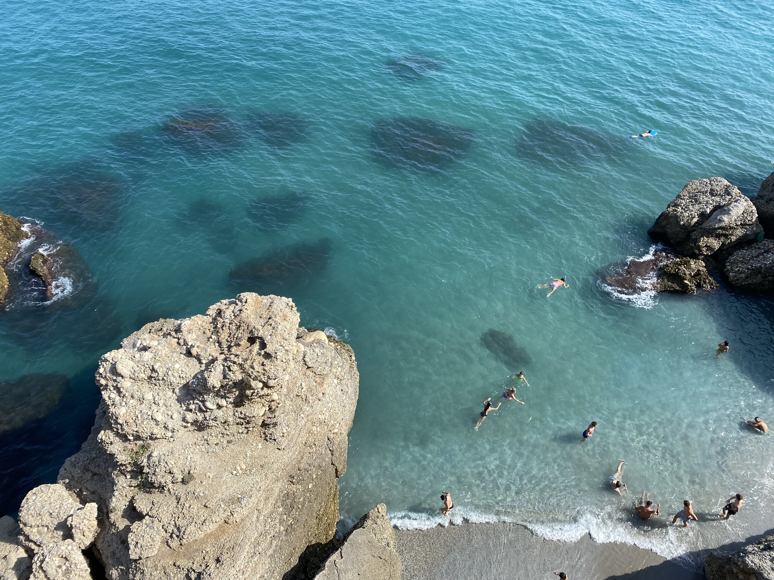 People swimming in clear blue ocean near rocky shoreline.