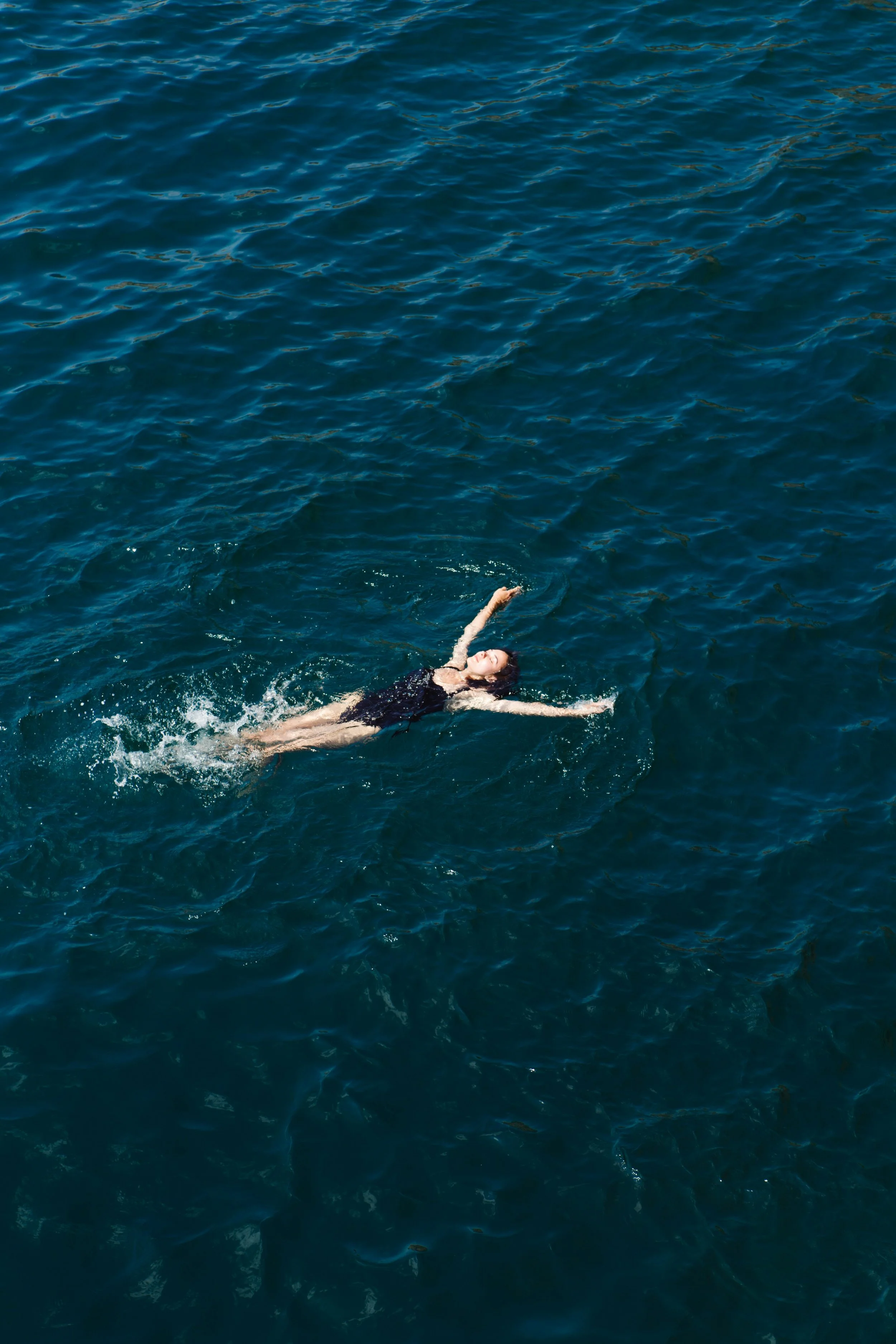 Person swimming in a large body of deep blue water with visible ripples.