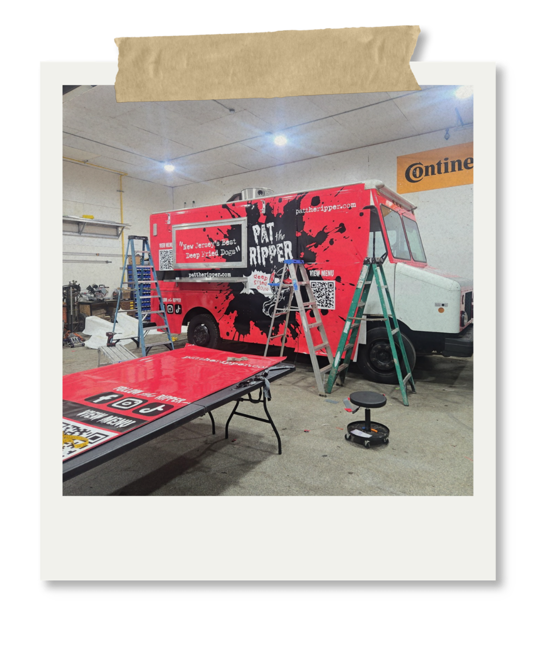 A food truck with red and black graphics, displaying the name 'Pat the Ripper,' inside a garage or workshop with ladders and tools around.