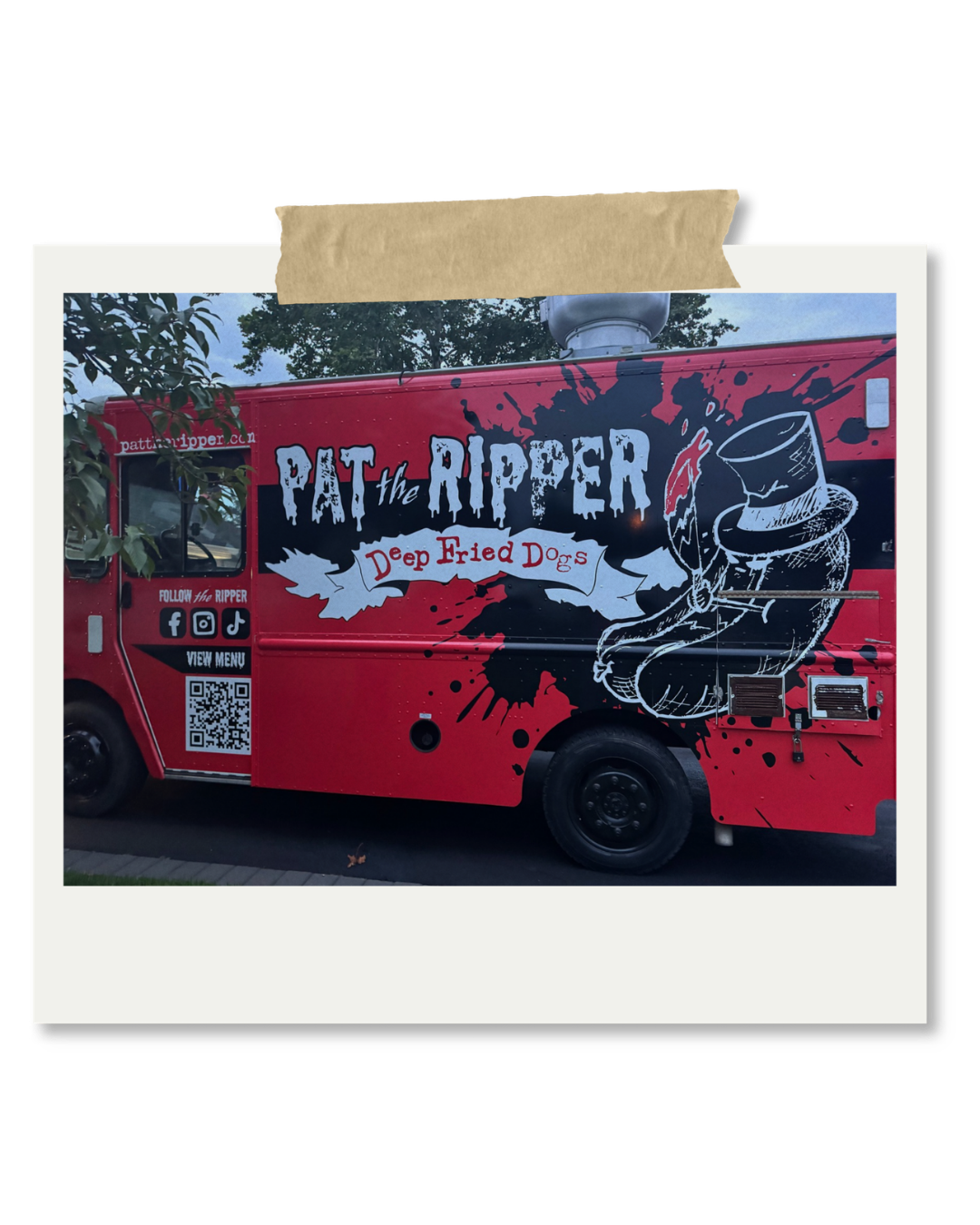 Red food truck labeled 'Pat the Ripper Deep Fried Dogs' with a black, white, and red graphic of a meat cleaver and splashes of black ink, parked outdoors with trees in the background.