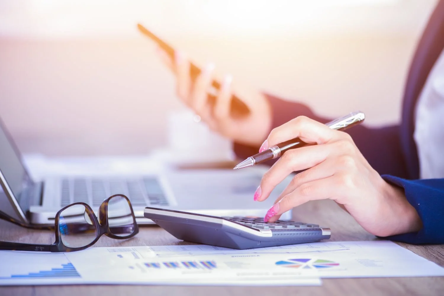 Person using a calculator with financial documents and a laptop on a desk.