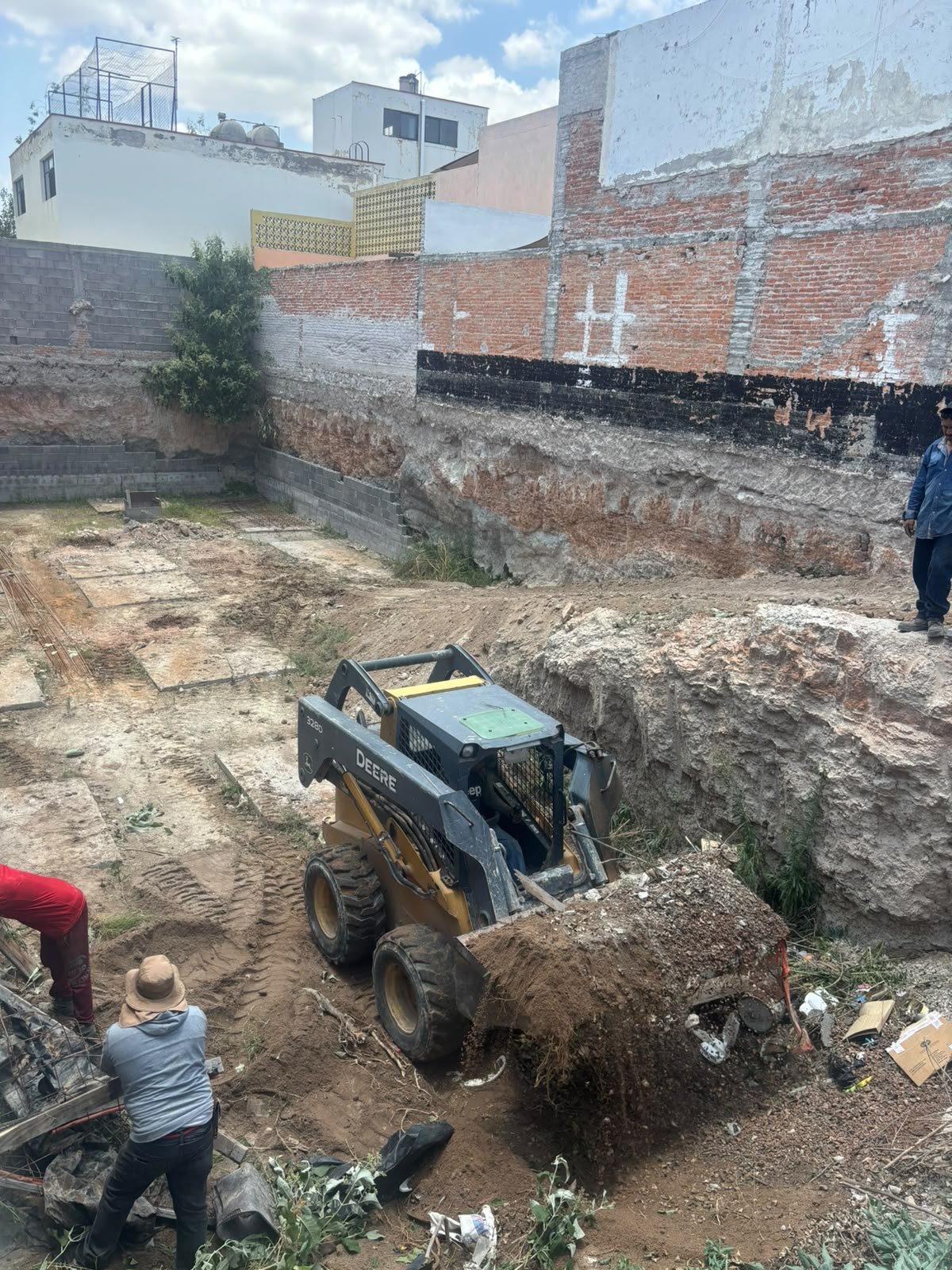 Excavación en un sitio de construcción con una mini cargadora amarilla y personas trabajando en el área