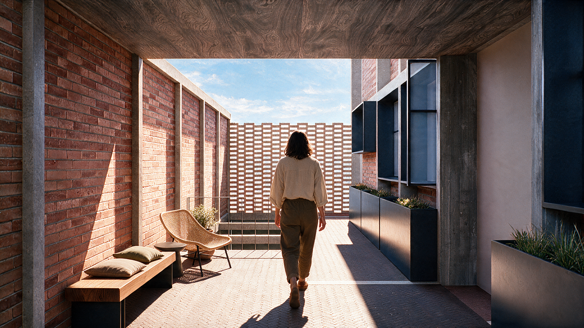 Persona caminando por un balcón con paredes de ladrillo rojo, decorado con muebles de madera, plantas en macetas y vistas al cielo azul con nubes.