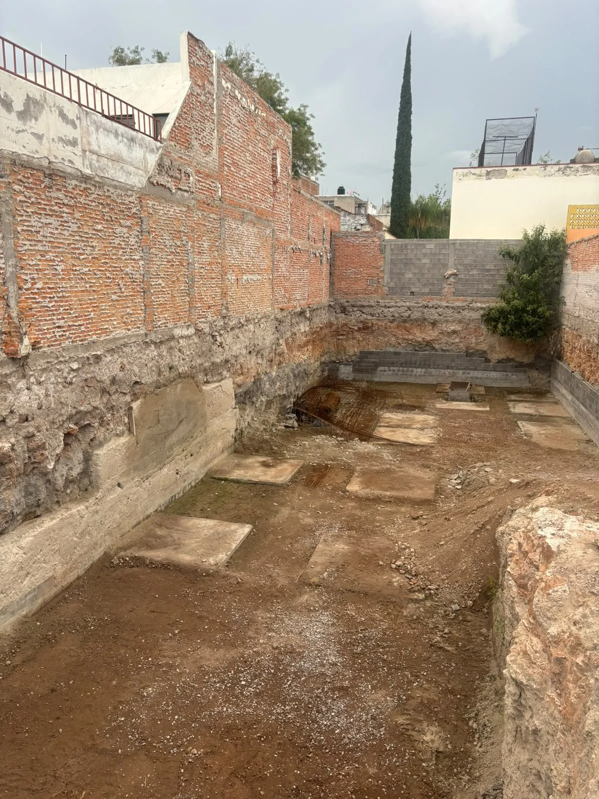 Sitio de construcción con cimientos excavados, muros de ladrillo y tierra, preparado para una edificación.