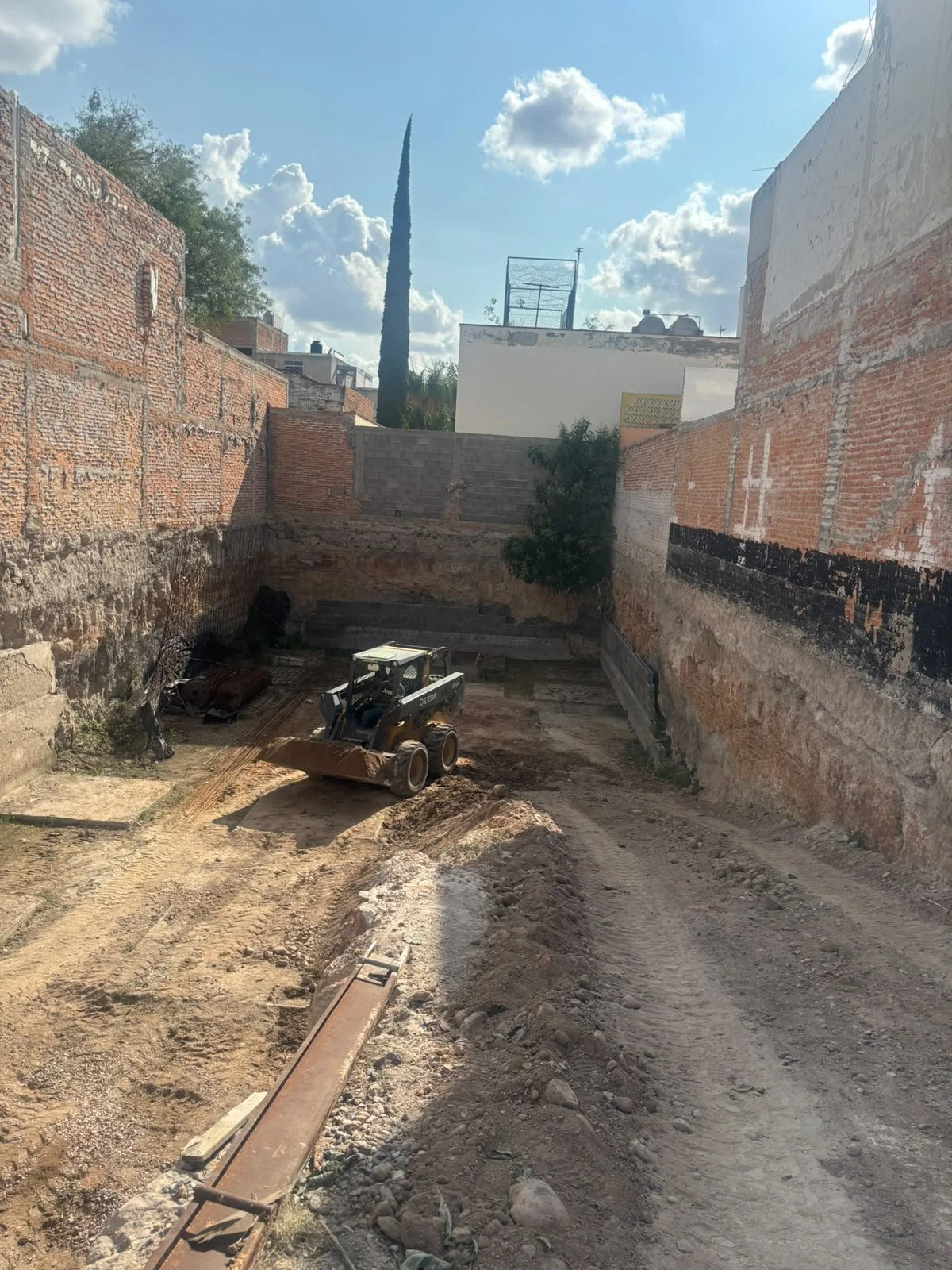 Construcción de un sótano o cimiento con maquinaria en un terreno excavado en una ciudad, con paredes de ladrillo y tierra expuesta.