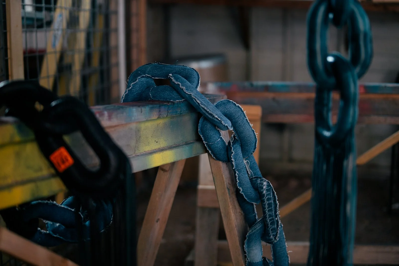 Textile artwork of a giant denim linked chain hanging on a wooden sawhorse in a garage or workshop.
