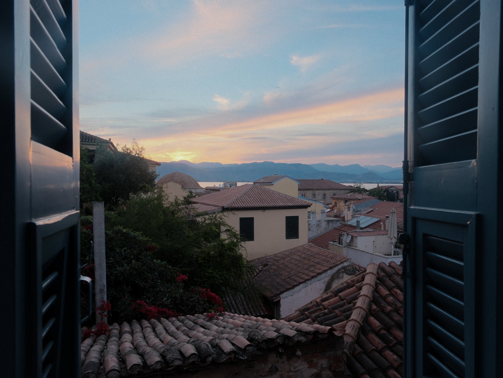 View of rooftops and mountains through blue window shutters during sunset