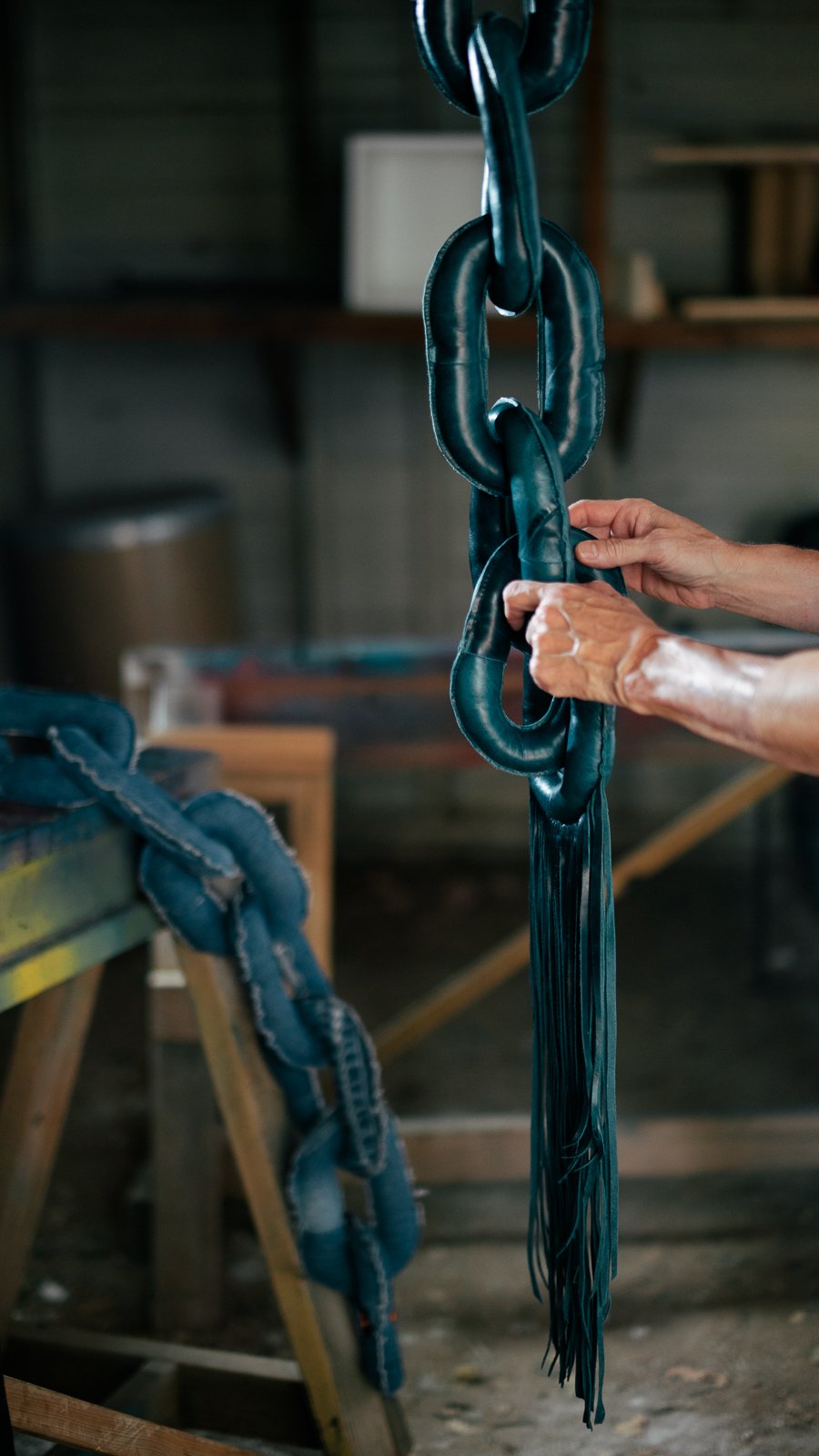 A person working on black leather strips, possibly for a craft or upholstery project, with tools and a workbench in the background.