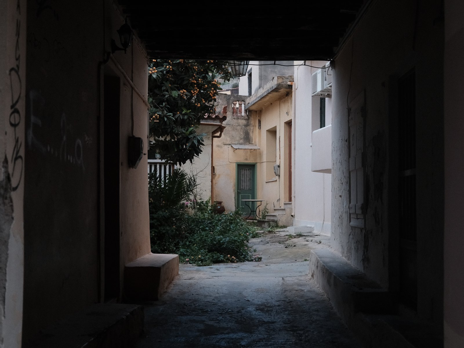 View of an alleyway with old buildings and plants, seen from a dark tunnel.