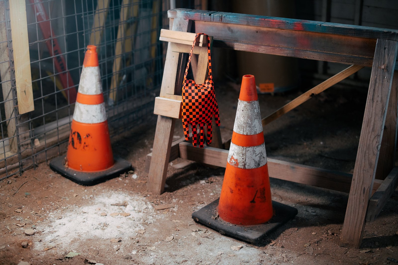 Construction site with two orange safety cones, a wooden barricade, a work glove hanging on a wooden frame, and a dirt floor.