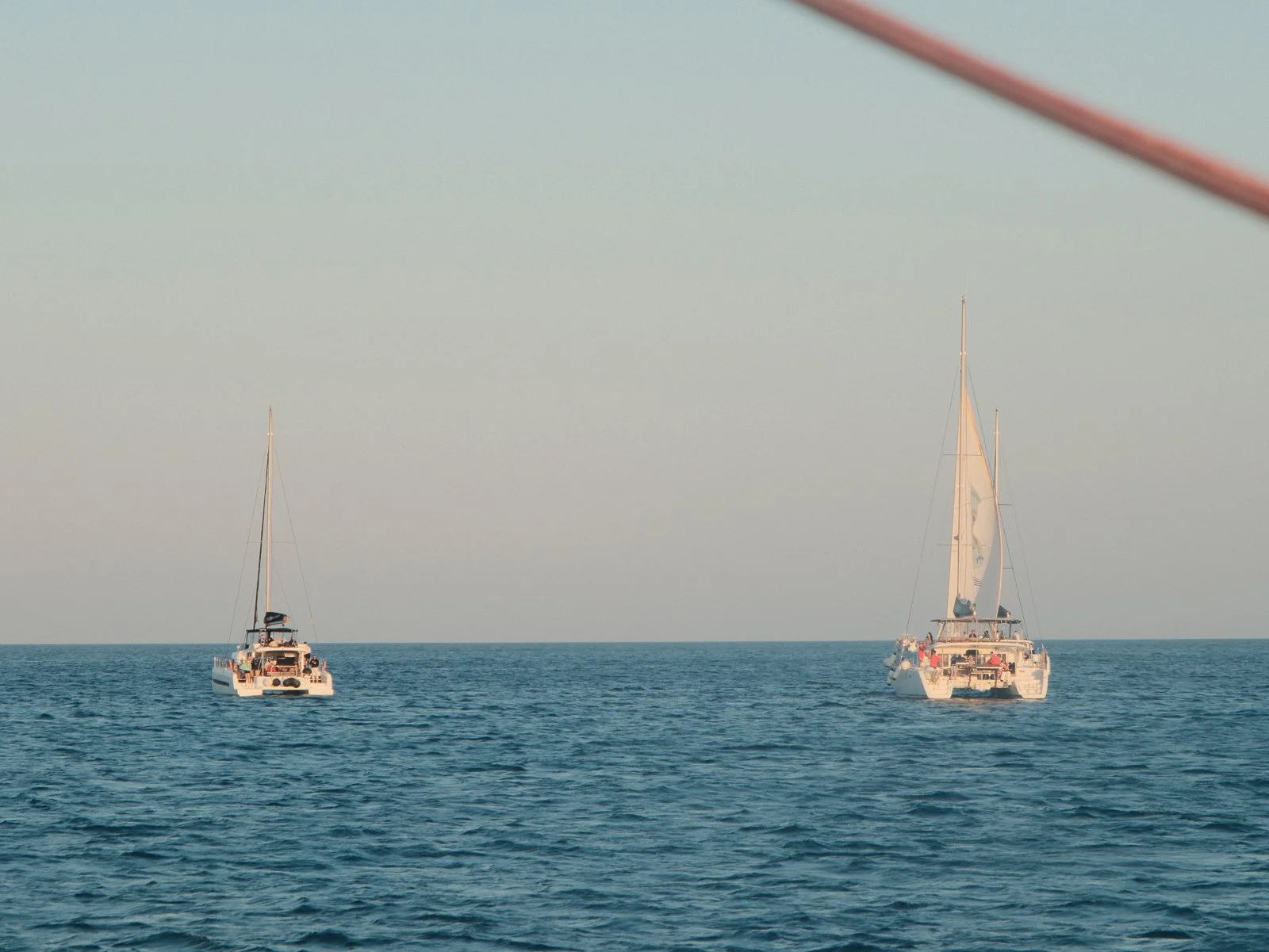 Two sailboats floating on calm ocean waters during sunset or sunrise.