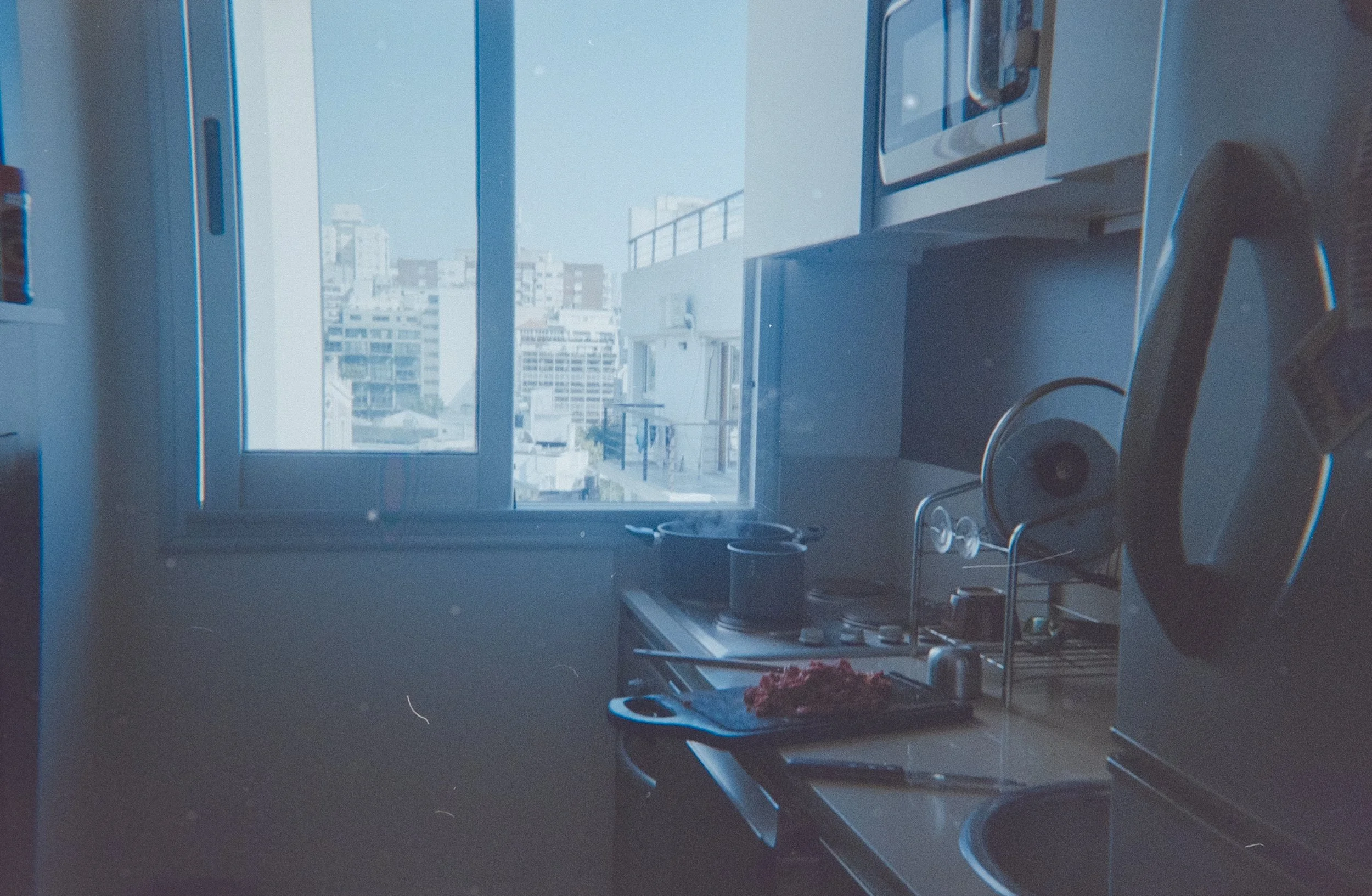 View of a city skyline through a large window in a room, with objects like headphones and a turntable on a table nearby.