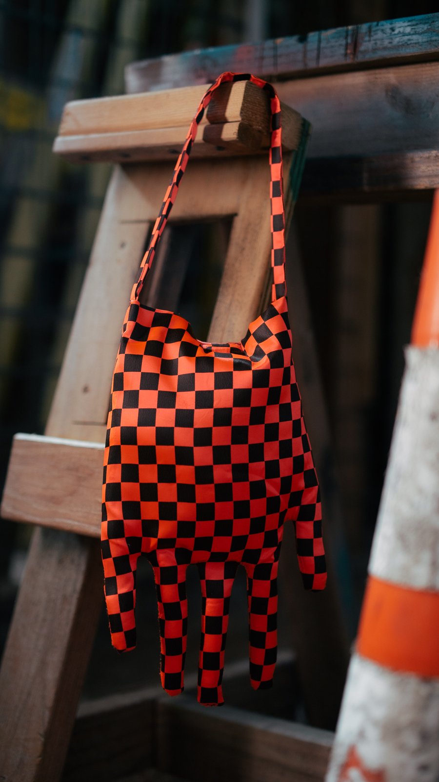 A tote bag with a red and black checkered pattern, designed to look like a hand, hanging from a wooden ladder.