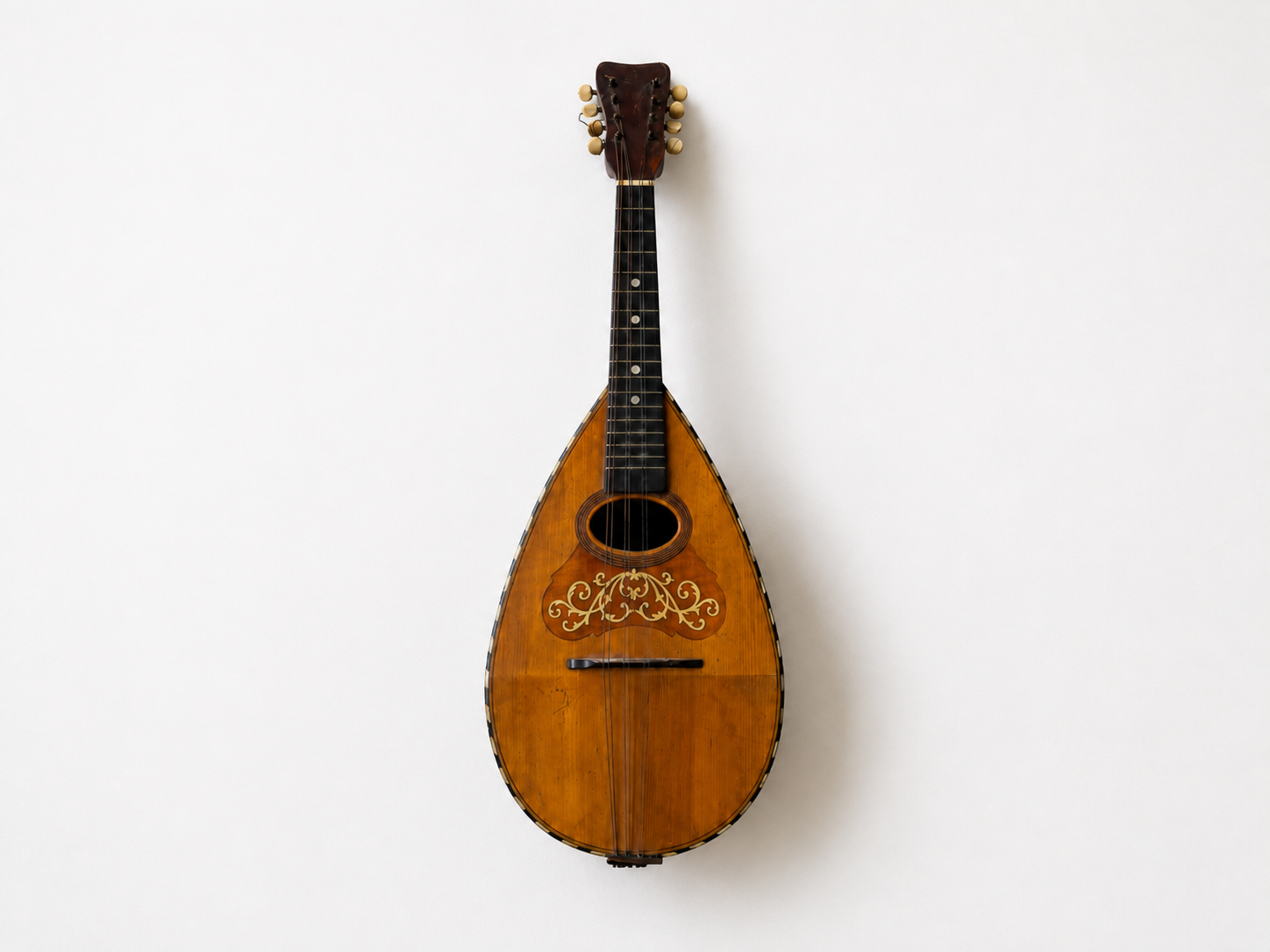 Guitarra clásica de madera con diseño decorativo en la parte frontal, colgada en una pared blanca.