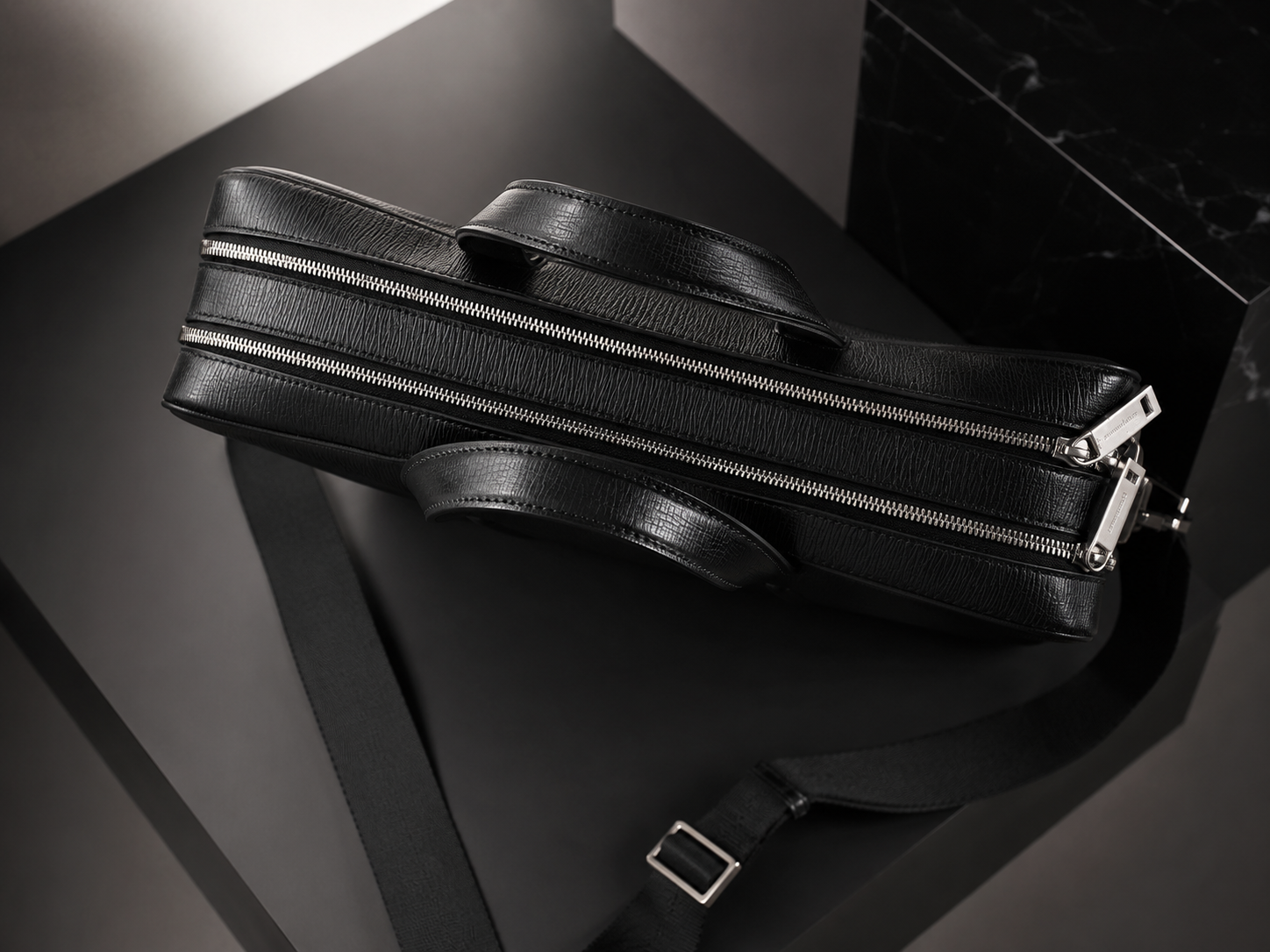Bolsa de cuero negra con múltiples cremalleras y correas, sobre una mesa negra