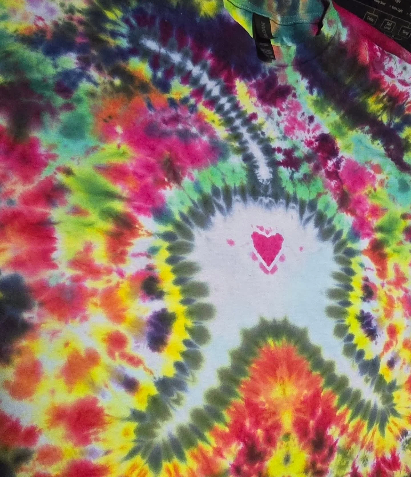 Close-up of a colorful tie-dye fabric with a white circle and pink heart design in the center.