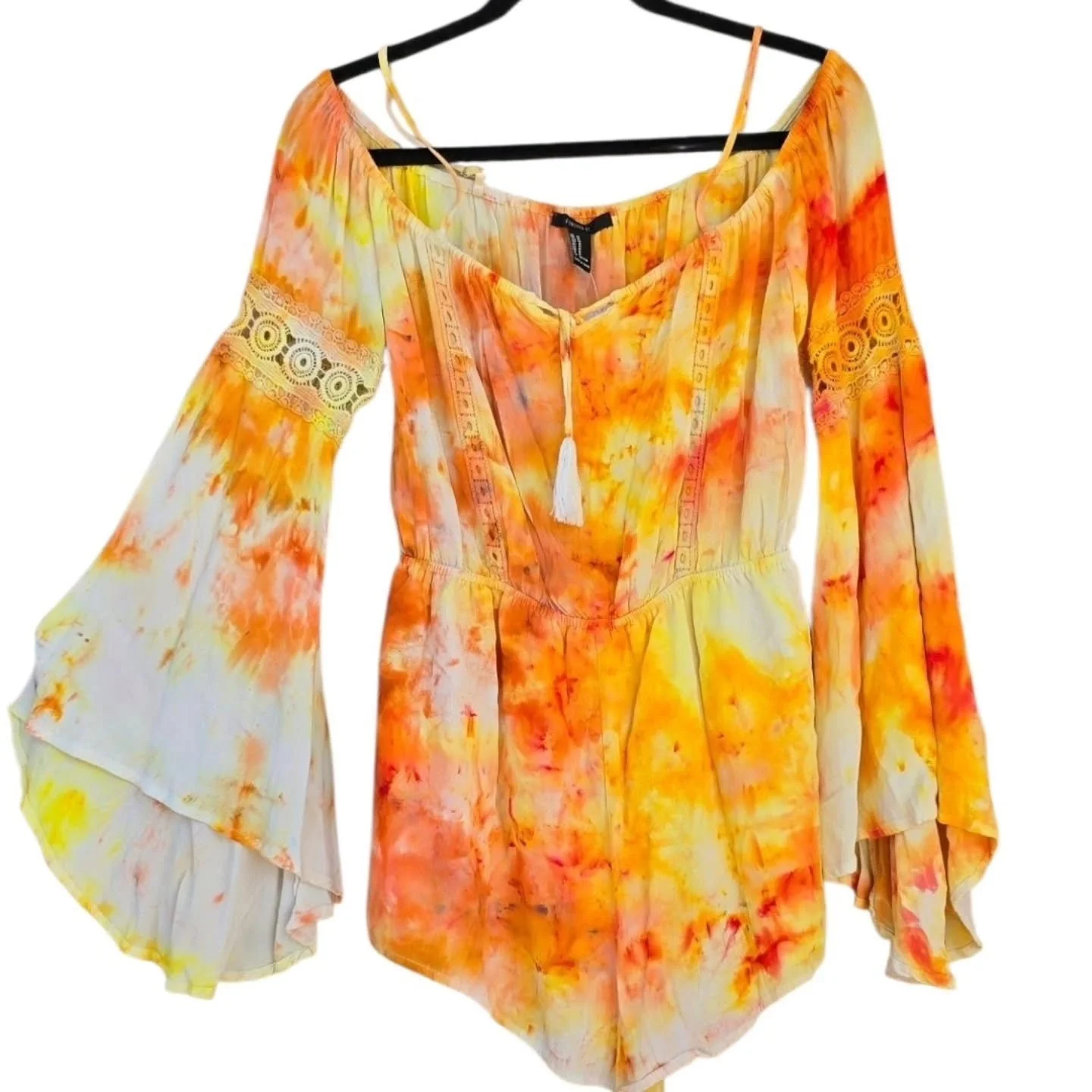 A colorful tie-dye dress with long, flowy sleeves and lace details on the upper sleeves, hanging on a black hanger against a white background.