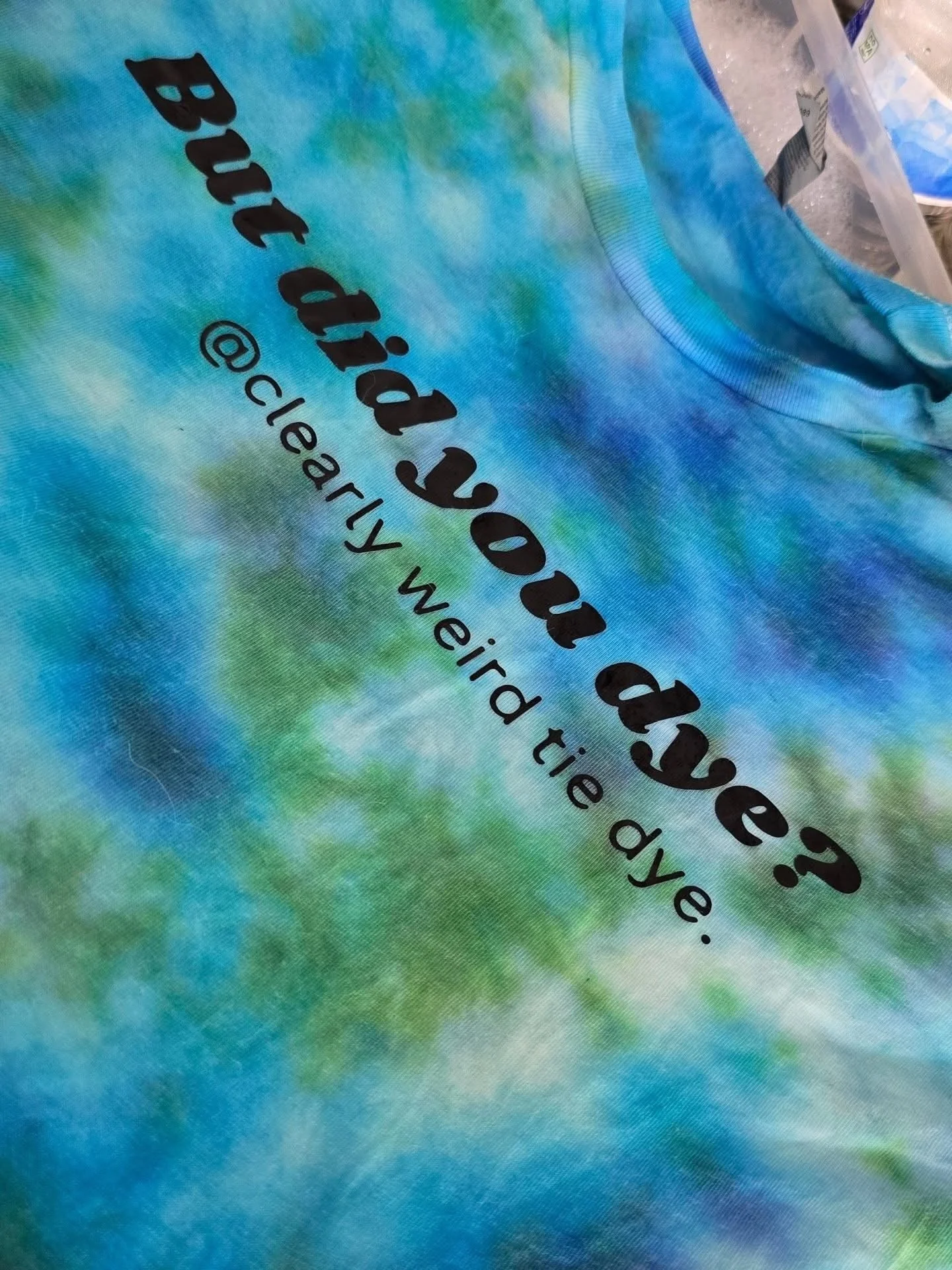Close-up of tie-dye fabric with text printed on it that reads 'but did you see? @cleararity_the_daye'.