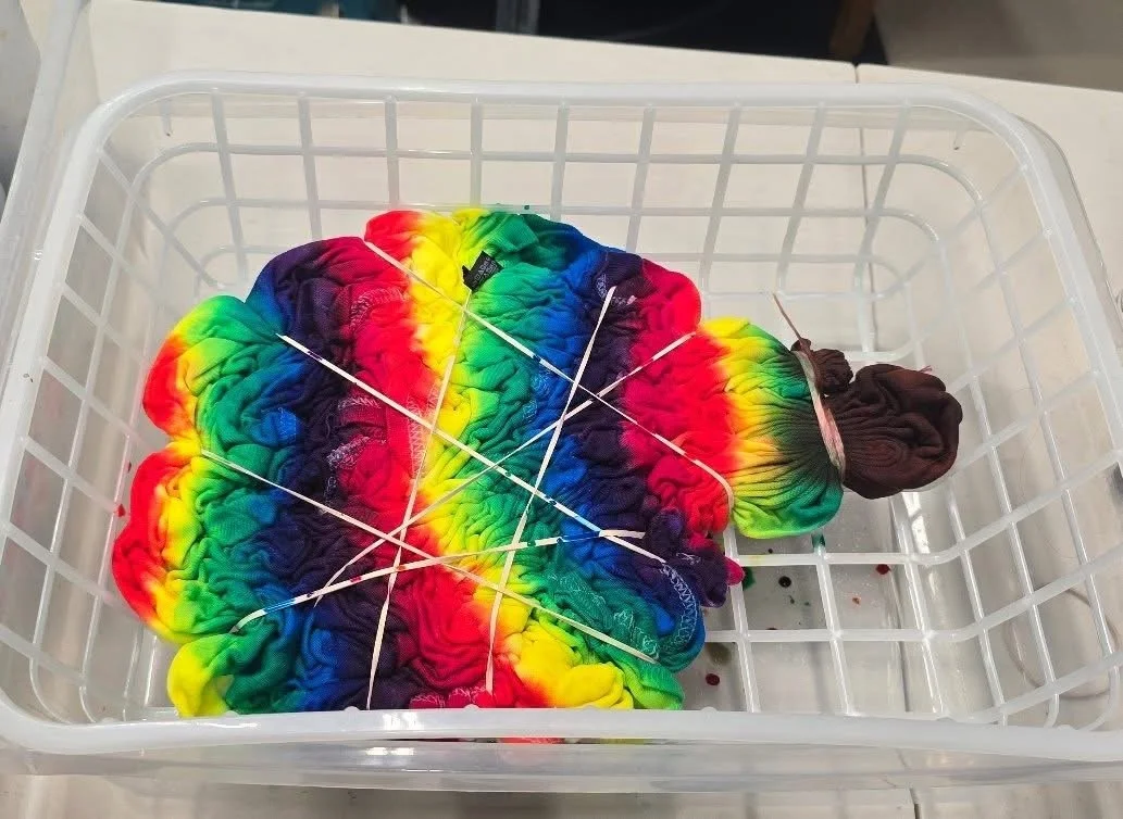 Colorful rainbow tie-dye fabric tied with rubber bands in a white laundry basket.