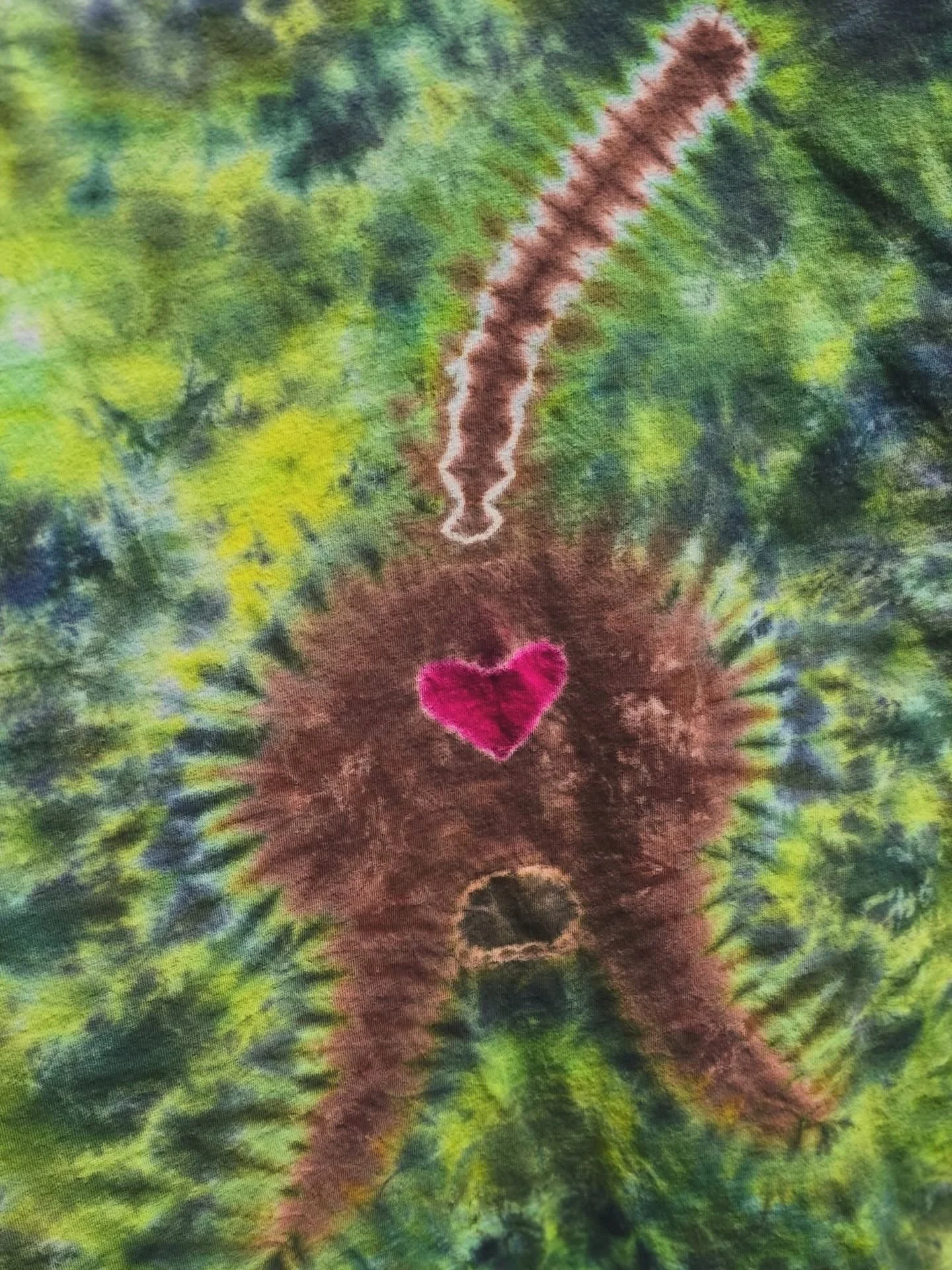Tie-dye fabric featuring a brown bear silhouette with a pink heart on its chest and a white zigzag line above it, set against a multicolored, tie-dye background.