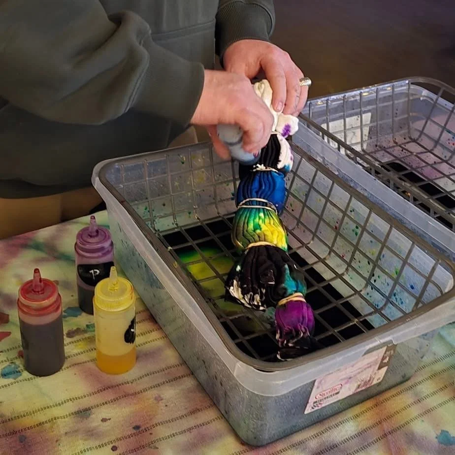 Person dyeing fabric yarns in a plastic container, with bottles of dye nearby.