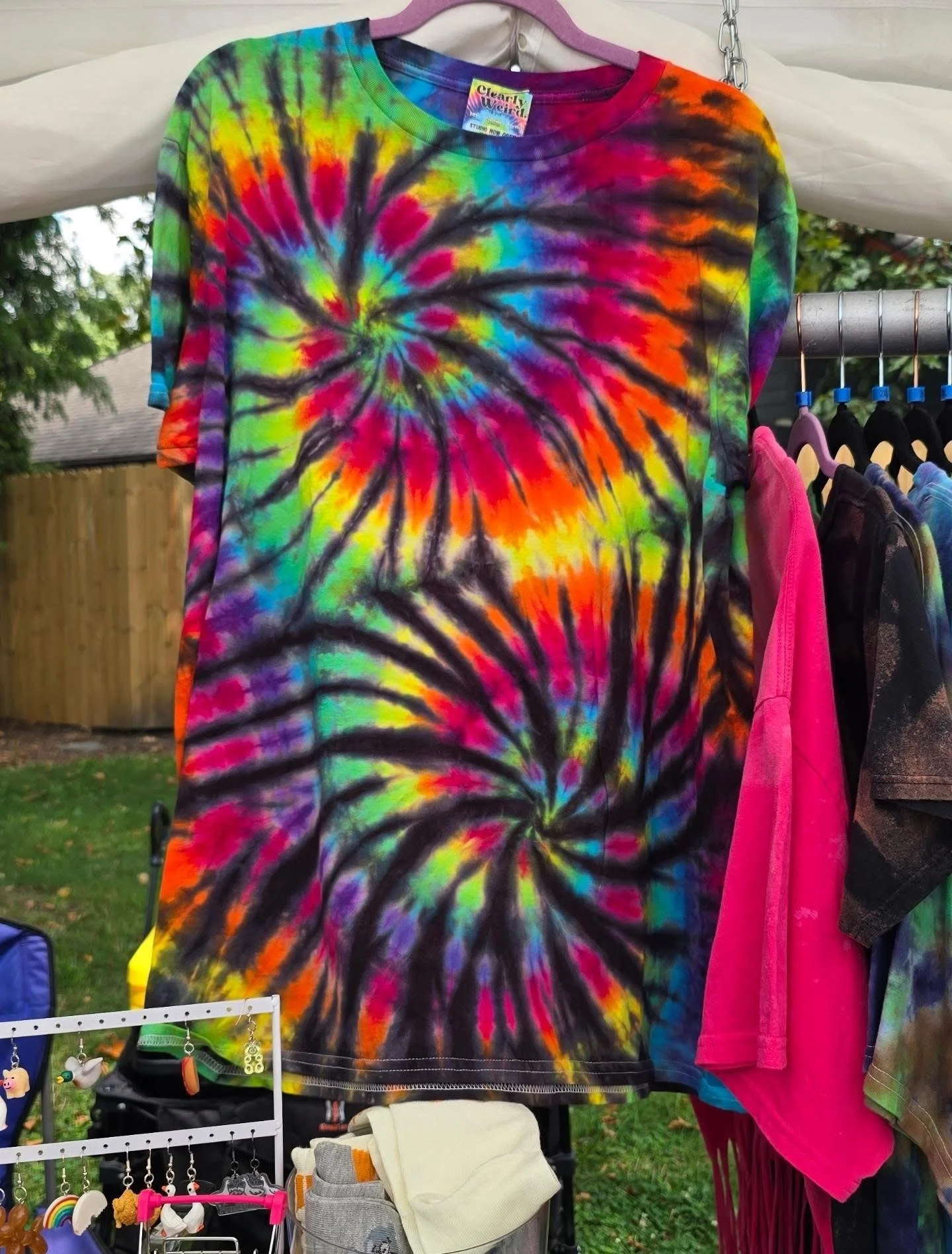 A tie-dye T-shirt with swirling bright colors hanging on a clothing rack outdoors.