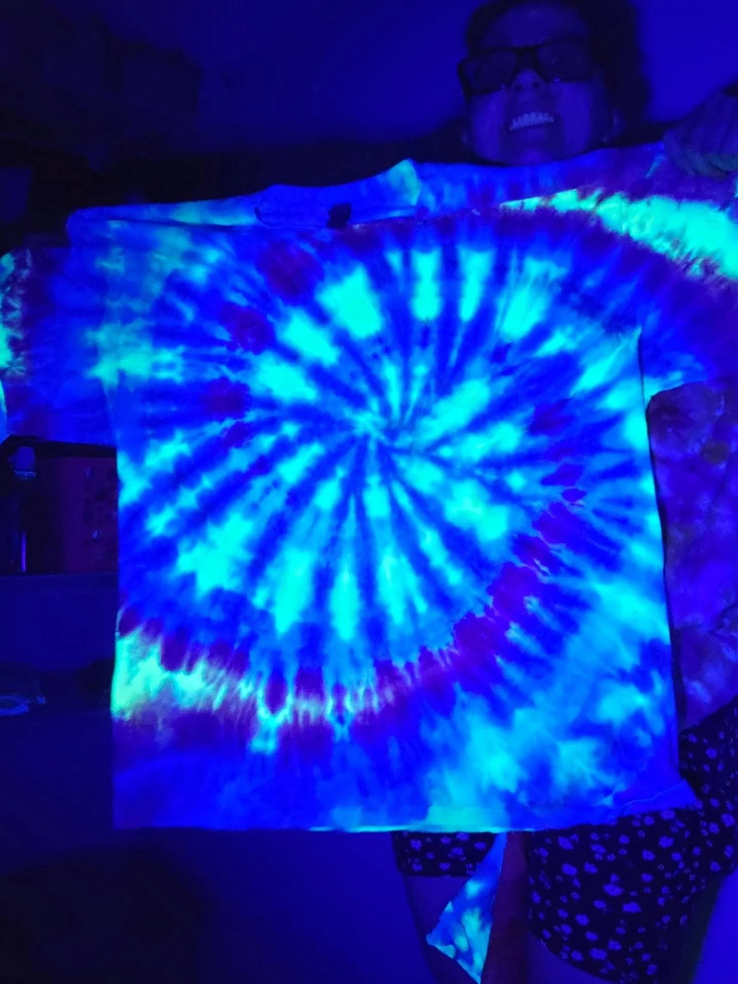 Person smiling and wearing glasses, illuminated by blue and white tie-dye light projection.