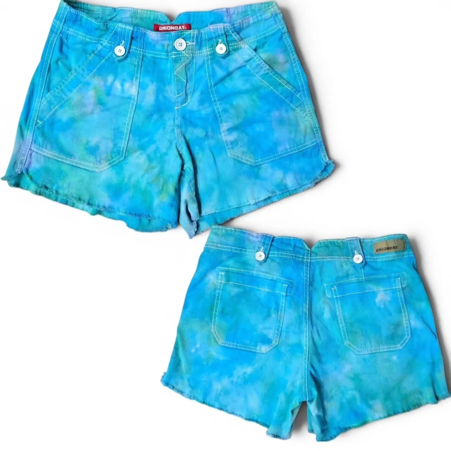 Two pairs of blue tie-dye shorts with white buttons, one with frayed edges, lying on a white surface.