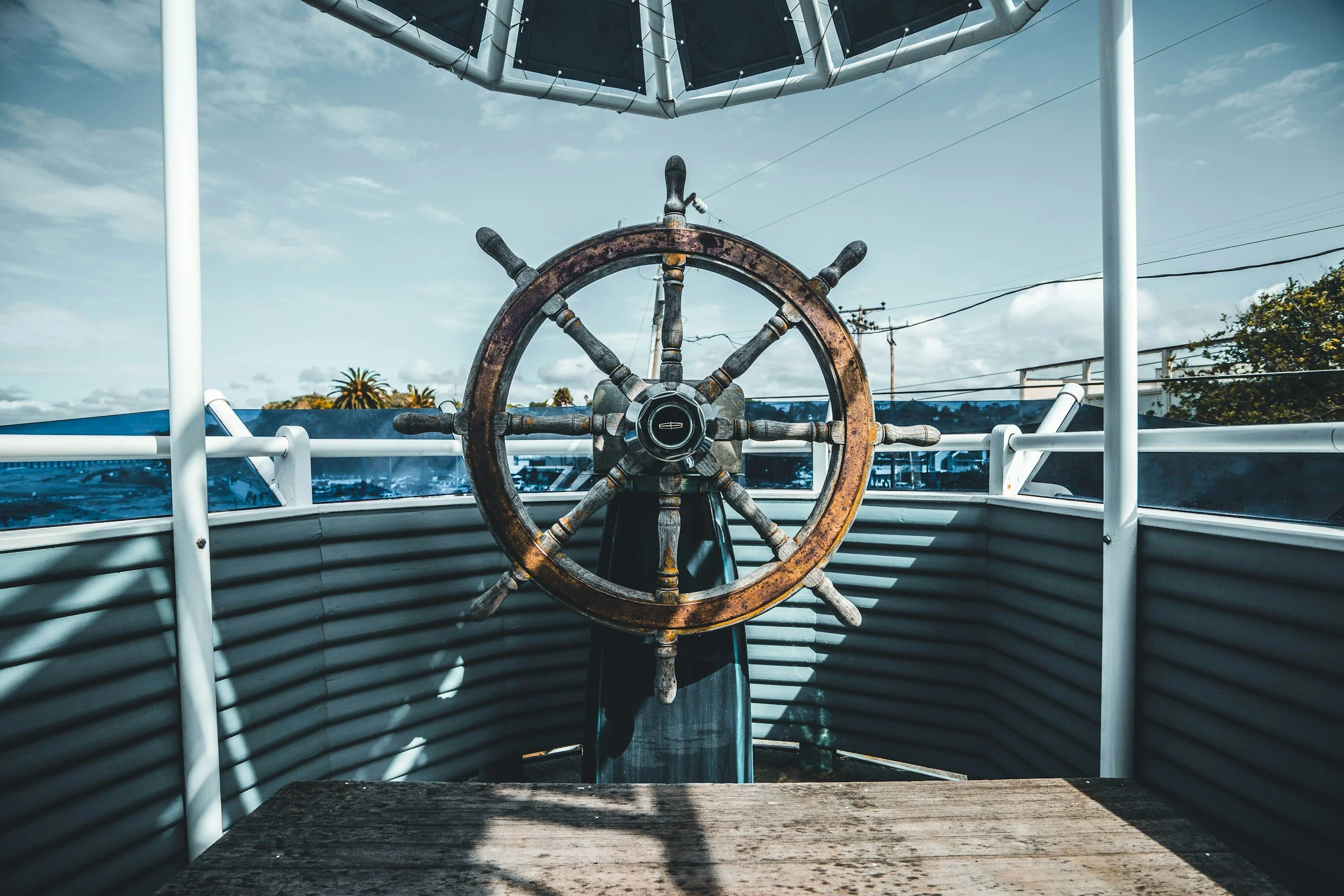 View from a boat's bow showing a rusty ship's wheel and the sky with some clouds, with trees and power lines in the background. Boat Captain for Hire
USCG Licensed Captain
Boat Delivery Captain
Yacht Delivery Captain
Captain for Hire NJ
Captain for H