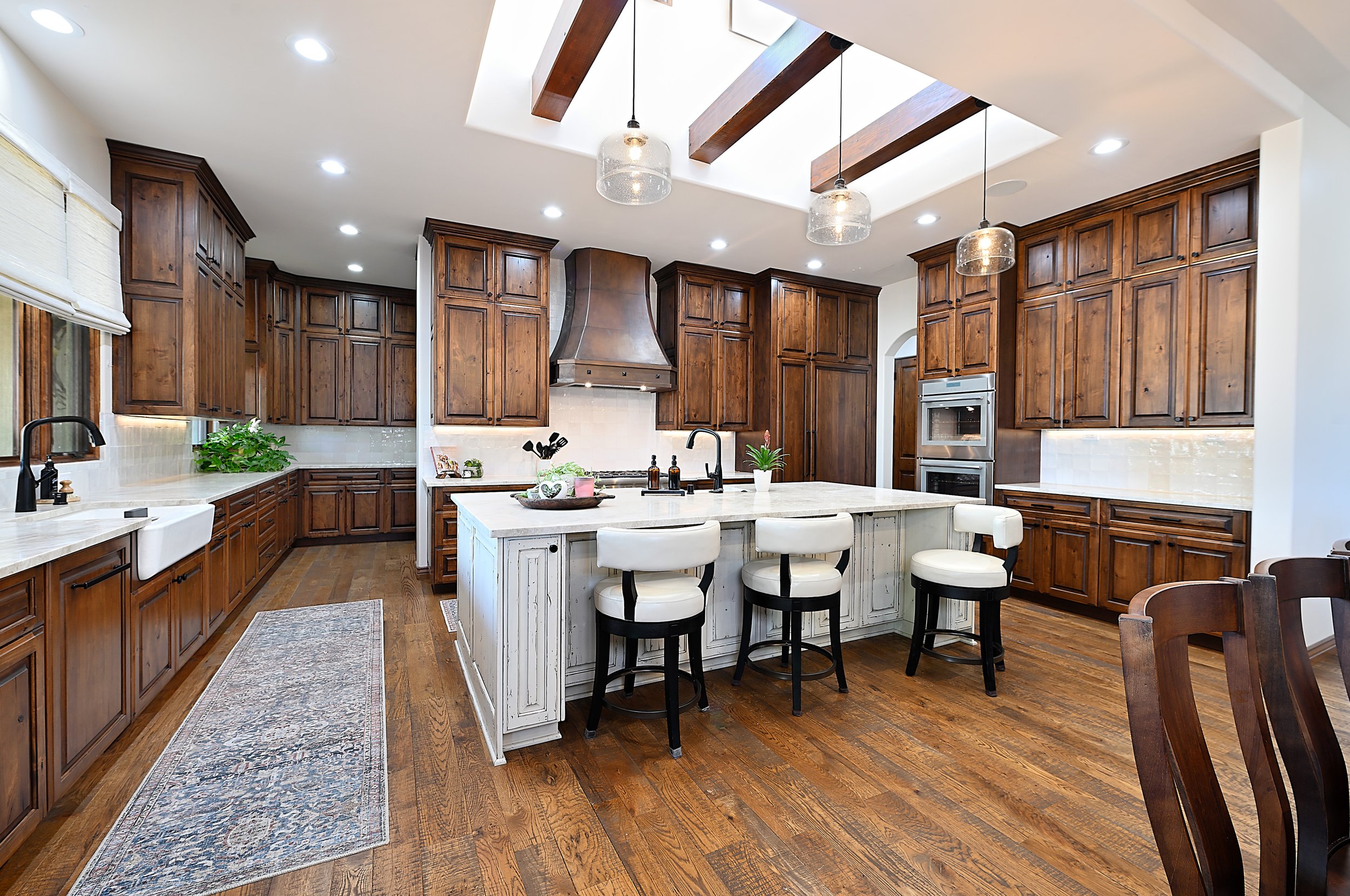 A spacious kitchen with wooden cabinets, a large white island with seating, pendant lights, and a skylight ceiling.