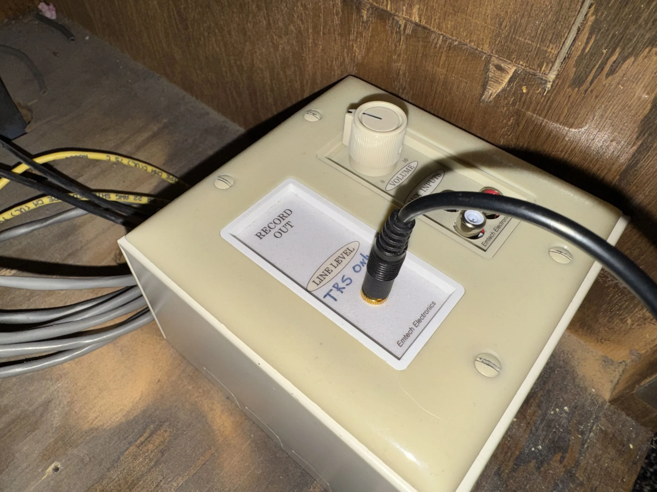 Close-up of a control panel with a volume knob, a switch, and several cables plugged in, mounted on a wooden surface.