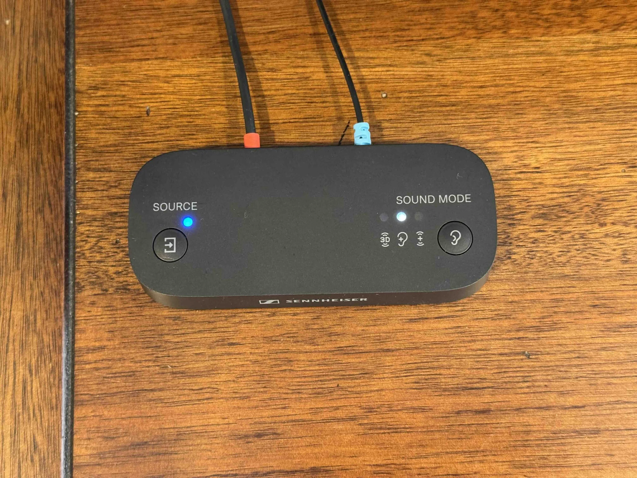 A black Sennheiser audio device on a wooden surface with two cables plugged into it.